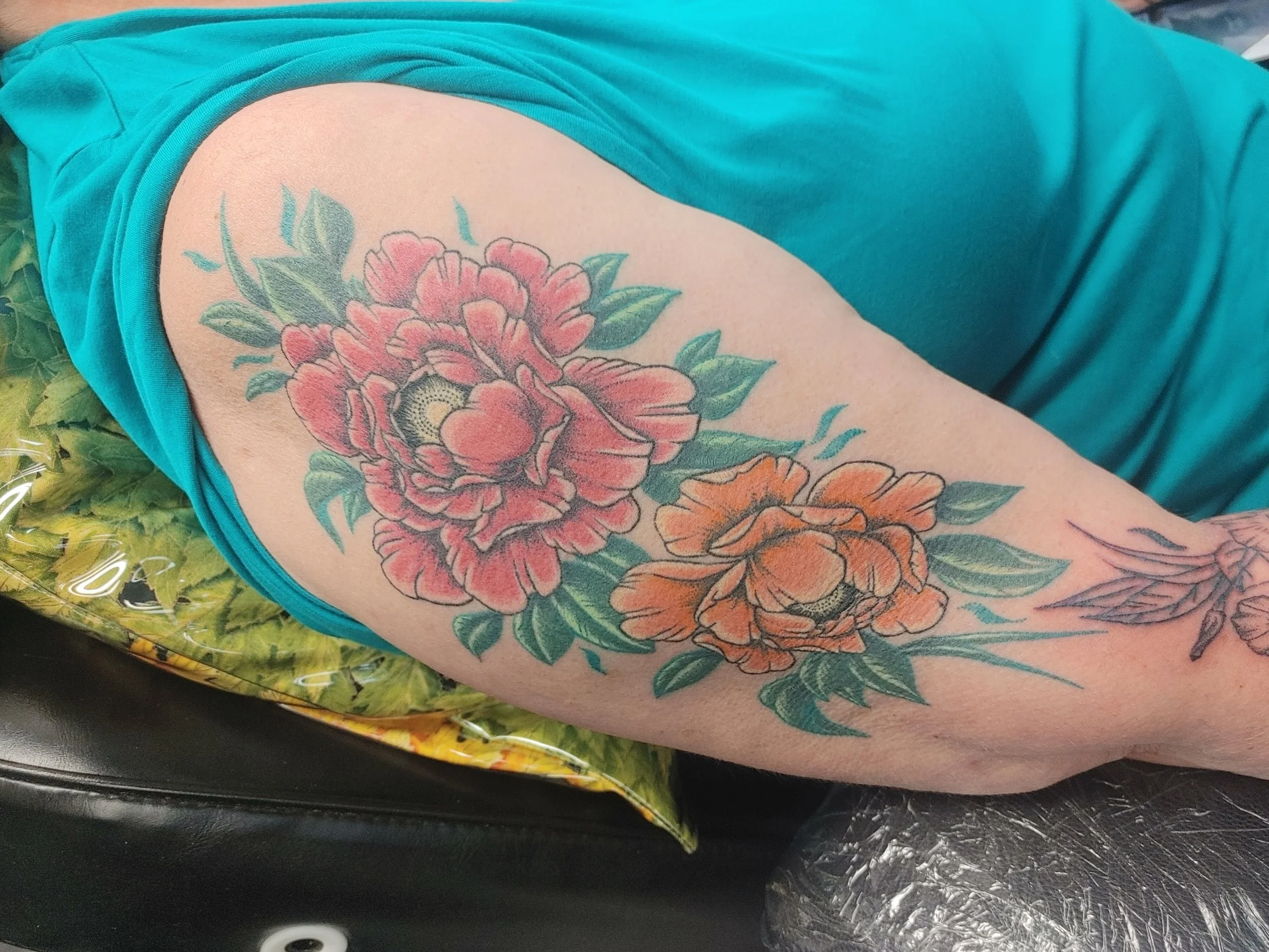 A person's upper arm with a large, colorful floral tattoo featuring pink and orange flowers with green leaves.