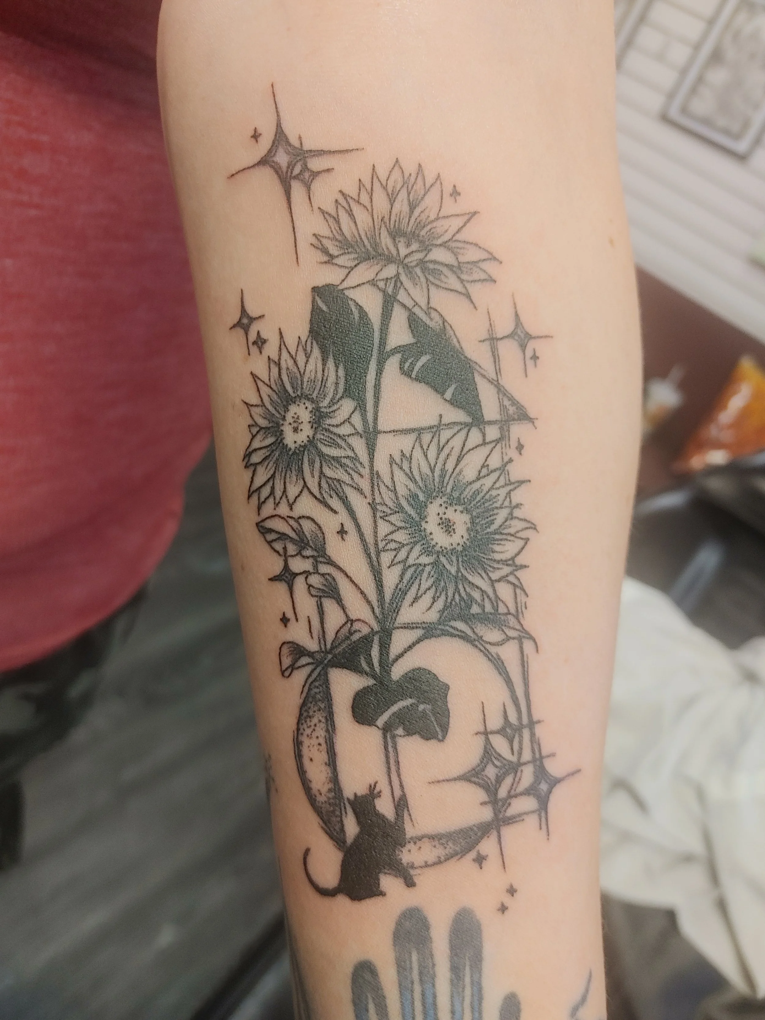 Tattoo of sunflowers, a cat, and stars on a person's arm.