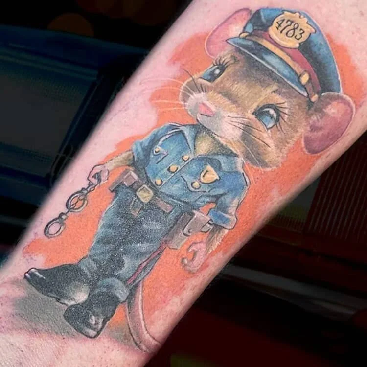 Tattoo of a cute mouse dressed as a police officer, wearing a police hat with badge number 4783, holding hand cuffs and a baton.