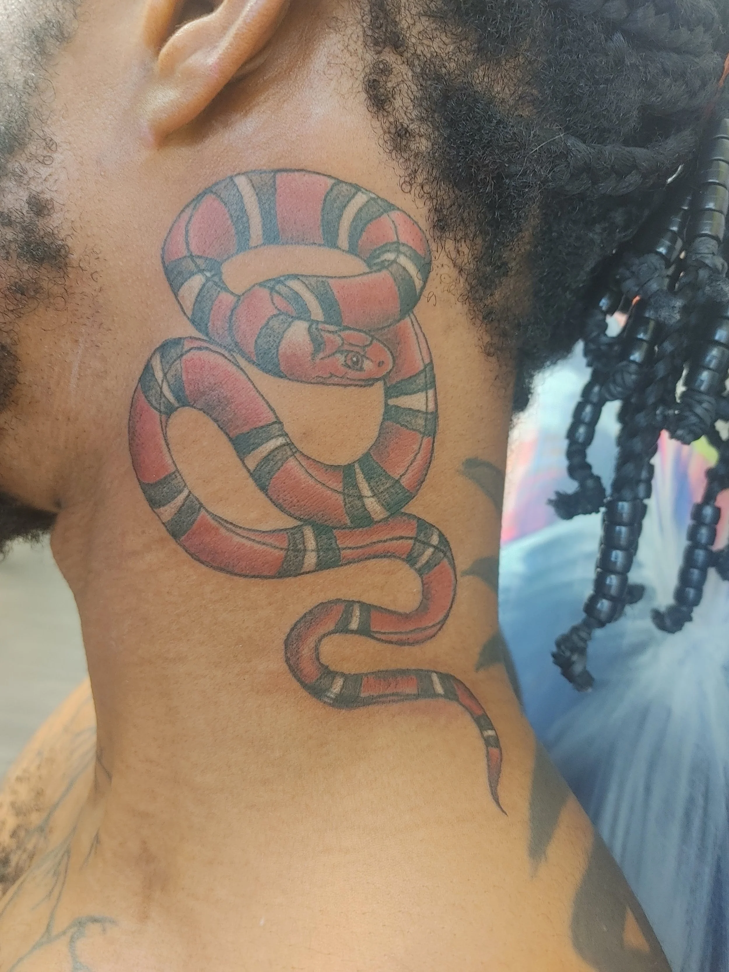 Close-up of a person's shoulder with a colorful snake tattoo and some curly hair.