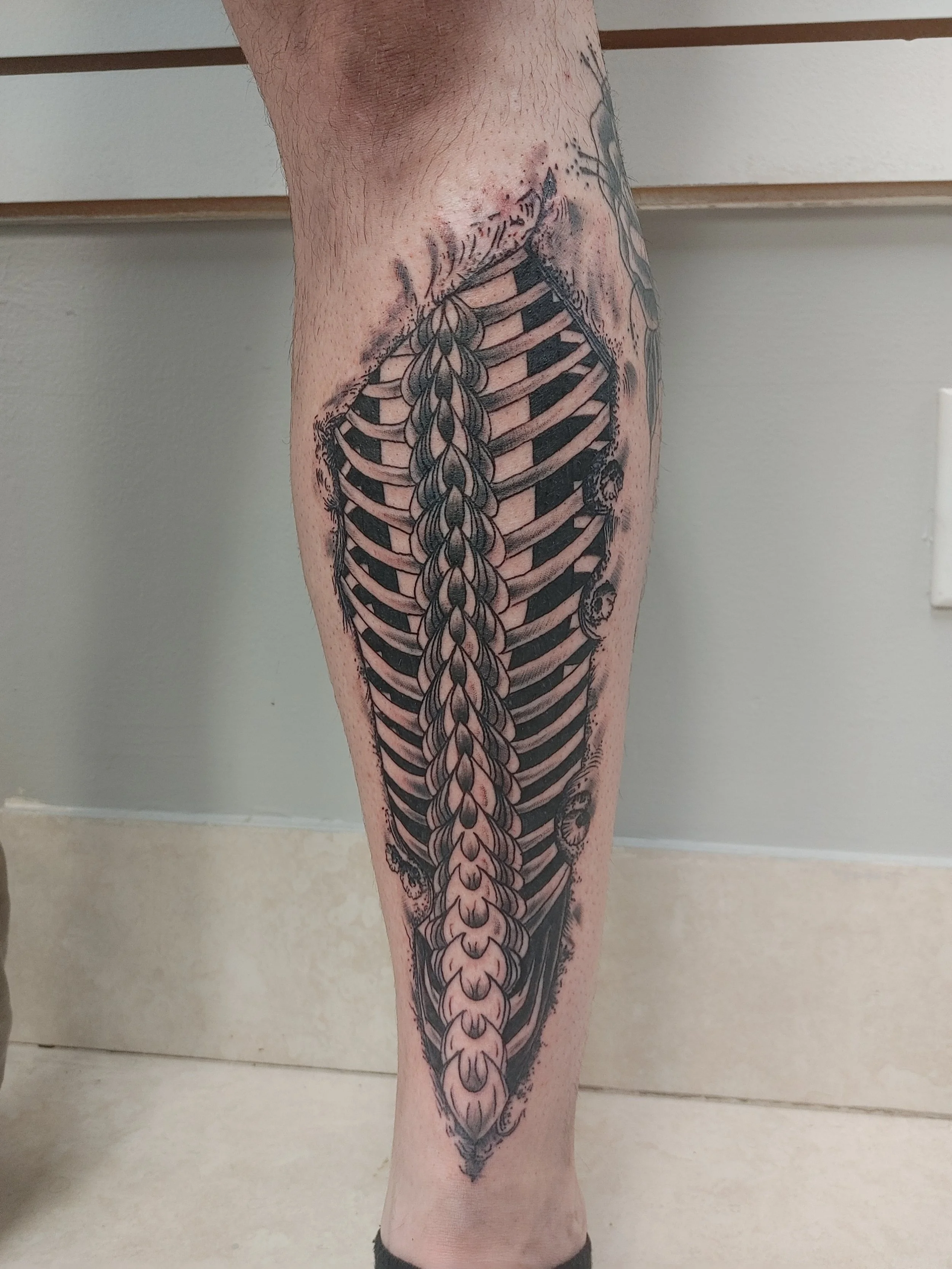 A tattoo on a person's leg depicting a detailed black and gray ship's skeletal structure, with intricate shading and line work.