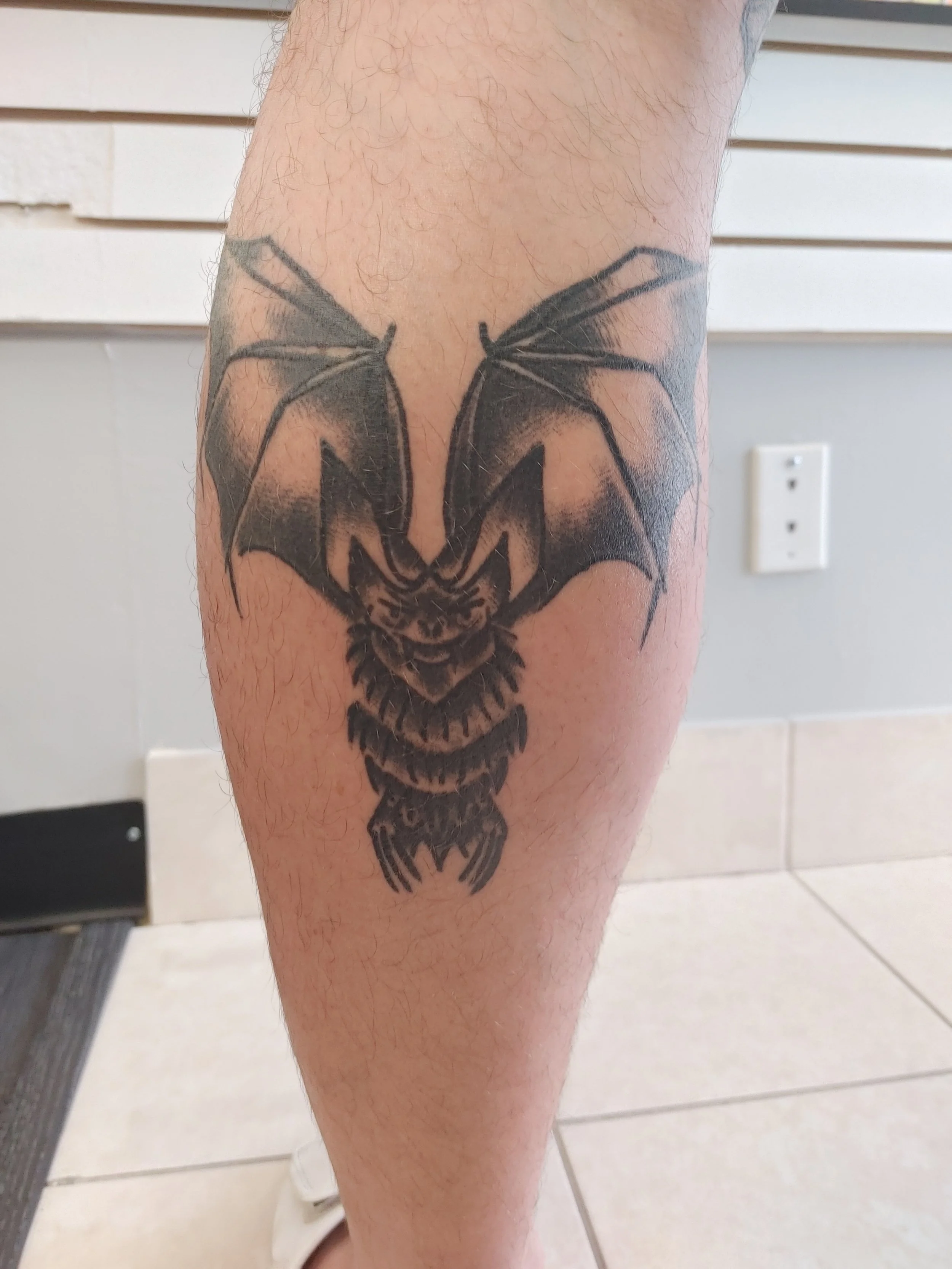 Tattoo of a dragonfly with outstretched wings on a person's lower leg.