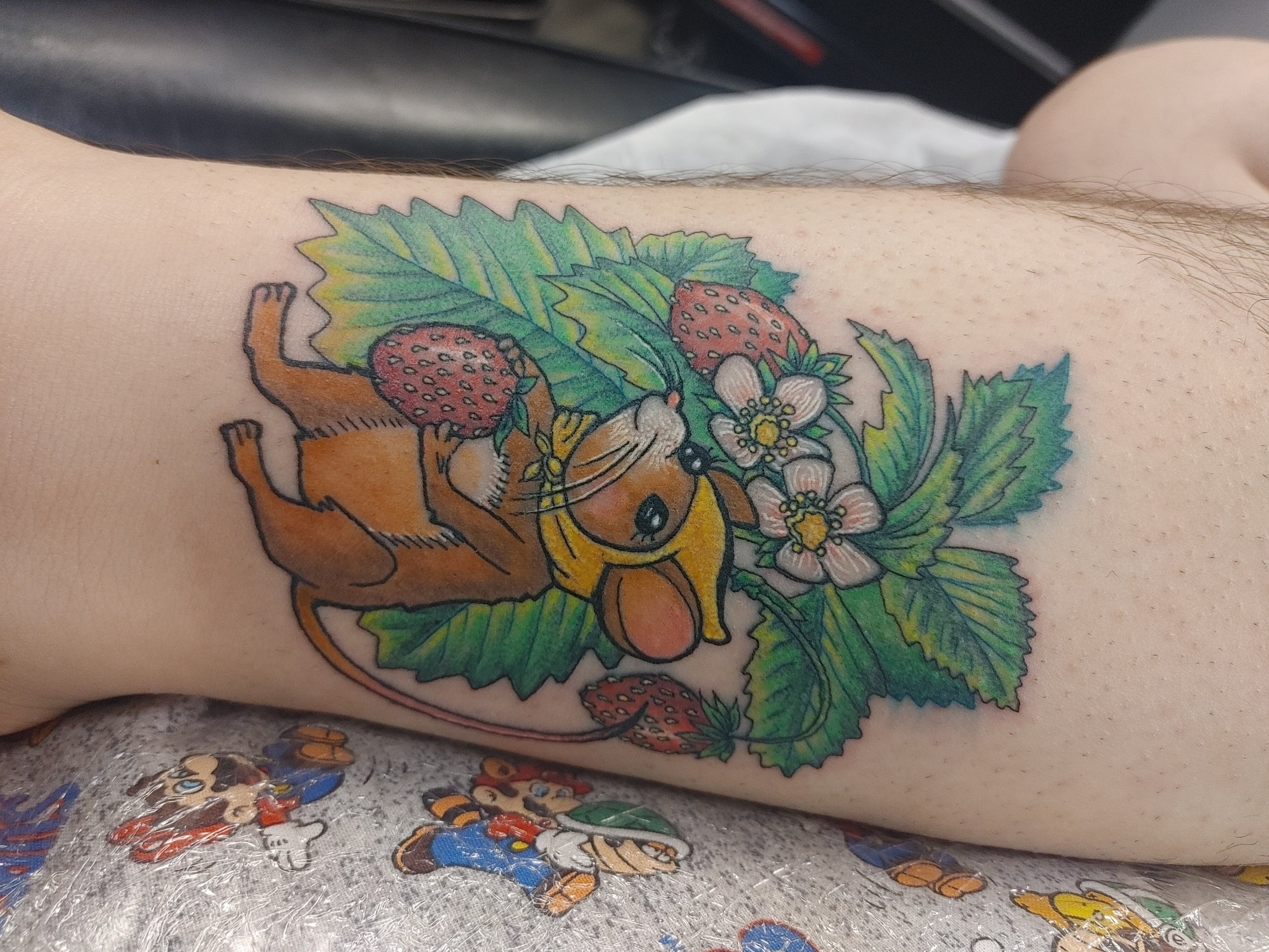 Colorful tattoo of strawberries, leaves, and flowers on a person's arm.