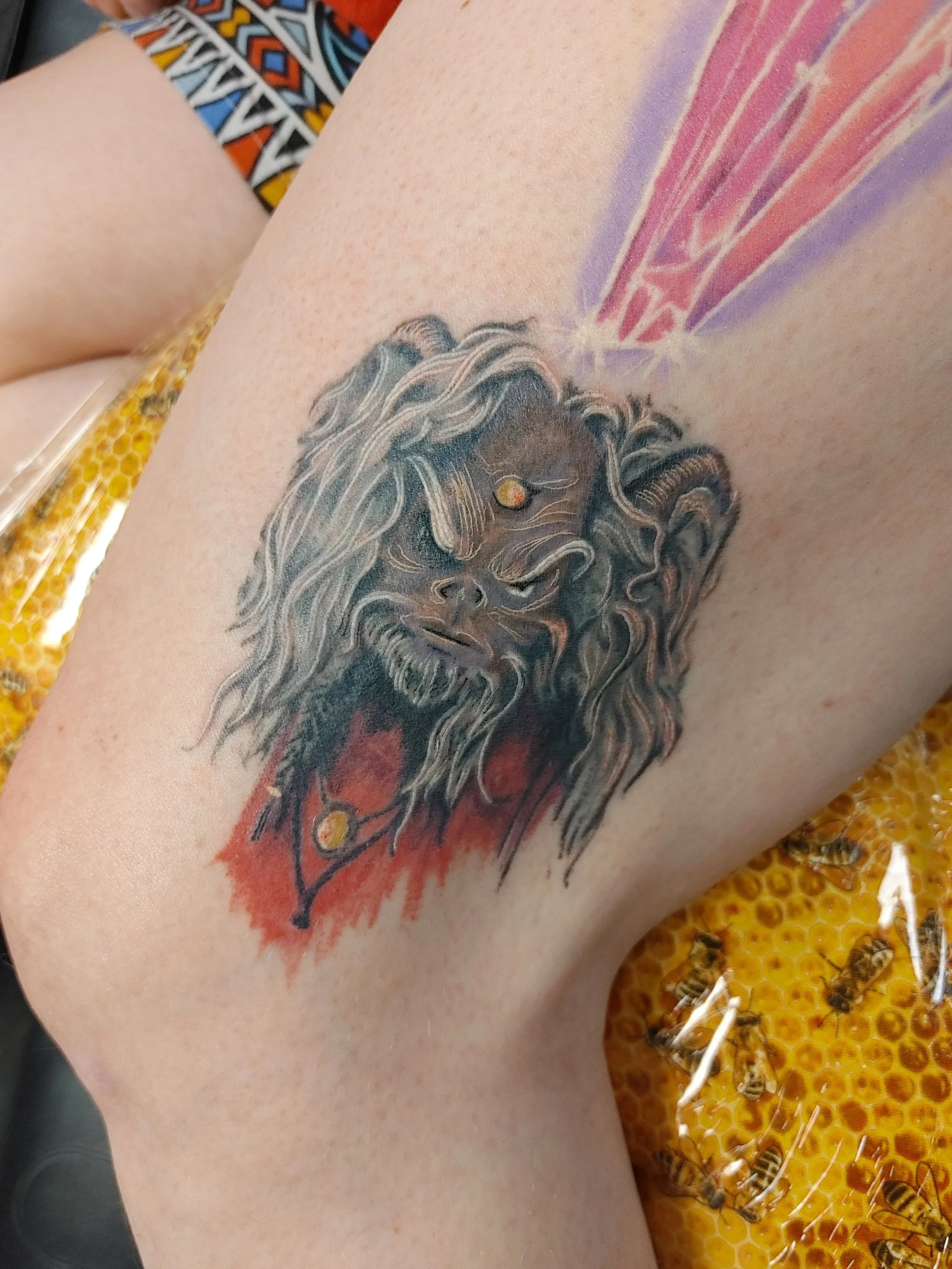 Close-up of a person's arm with a tattoo of a lion's face and supernatural wings, resting on honeycomb with bees.