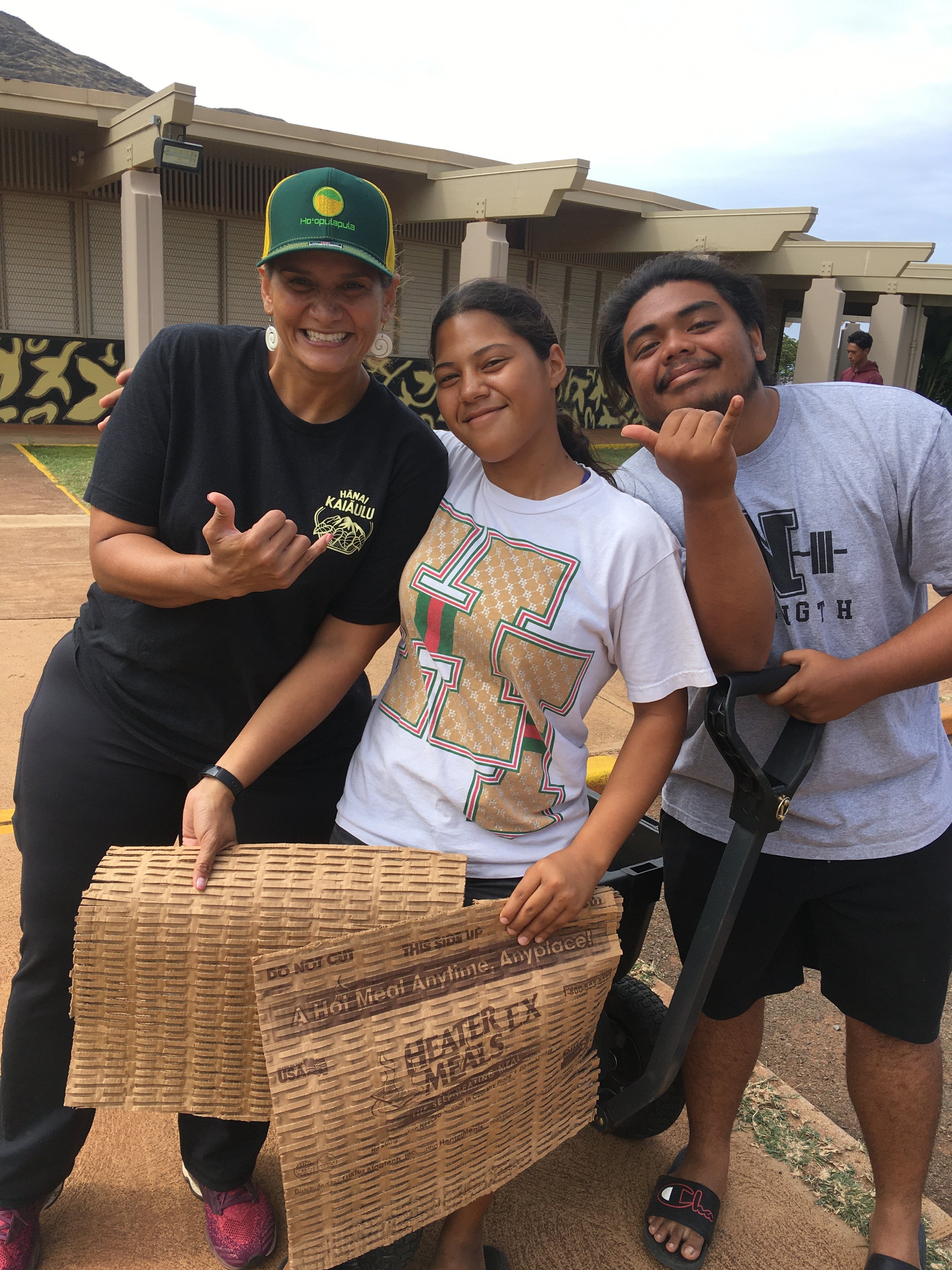 Two student participants in joyful smiles, making shaka hand gestures alongside their kumu.