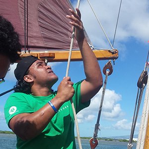 Kupu participant on a sailboat, actively pulling a rope during a sailing activity.