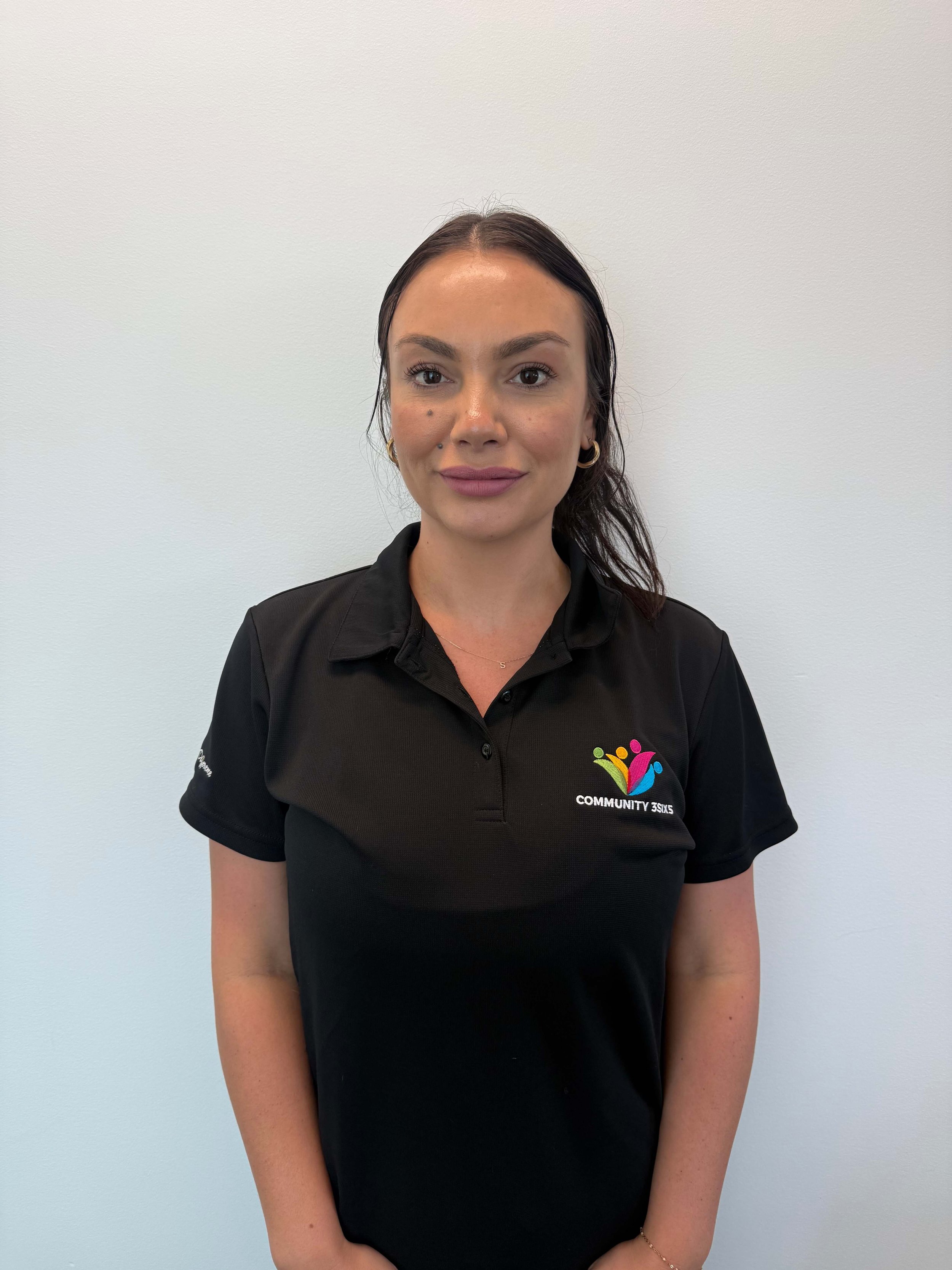 Mikka, a friendly Community3six5 disability support worker, smiling warmly at the camera in the black company polo uniform.