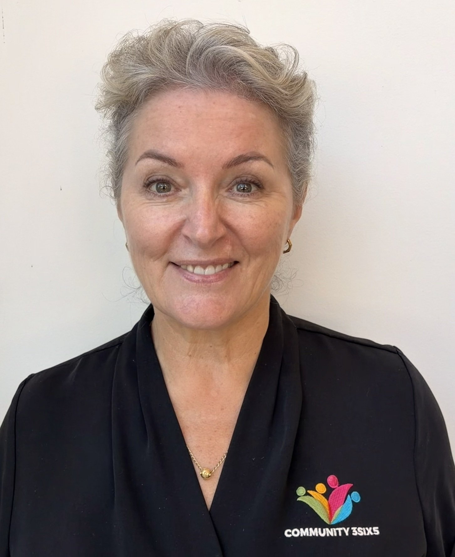 Female staff member Sally. Sally has grey/blonde hair in a ponytail. She is wearing a black polo uniform shirt and she is smiling.