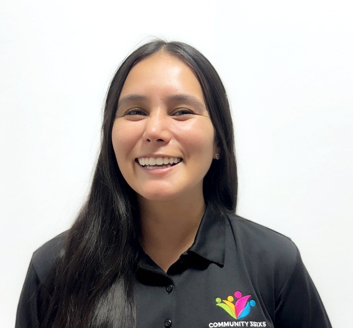 Female staff member Maria, she has long, straight, dark brown hair. She is wearing a black uniform polo shirt and she is smiling.