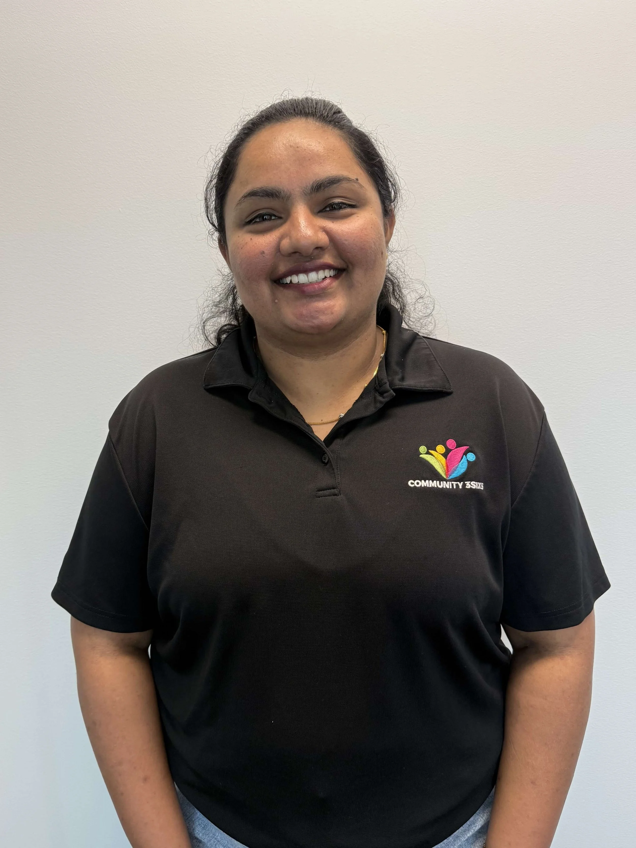 Sharon smiling while wearing a black Community3six5 polo uniform, representing community connection and support