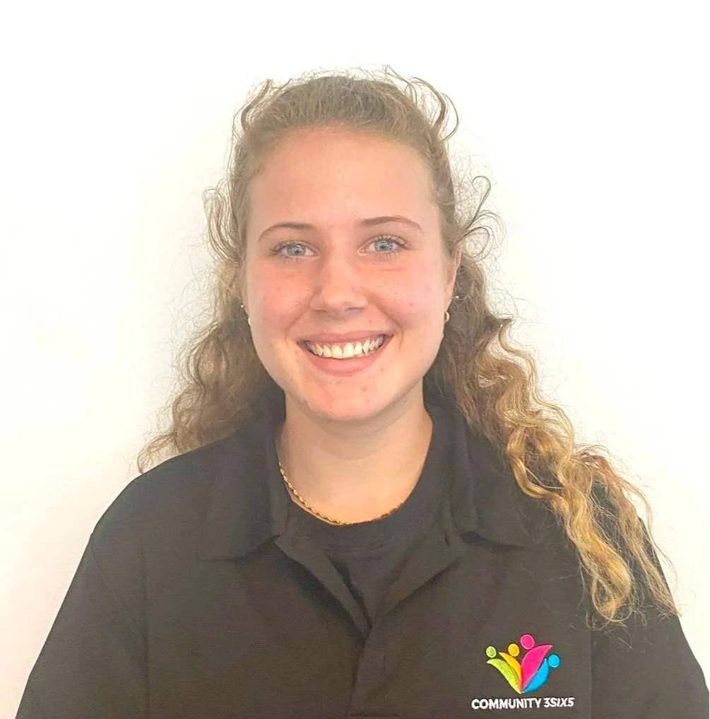 Female staff member Jessica K, she has long, curly blonde hair. She is wearing a black uniform polo shirt and she is smiling.