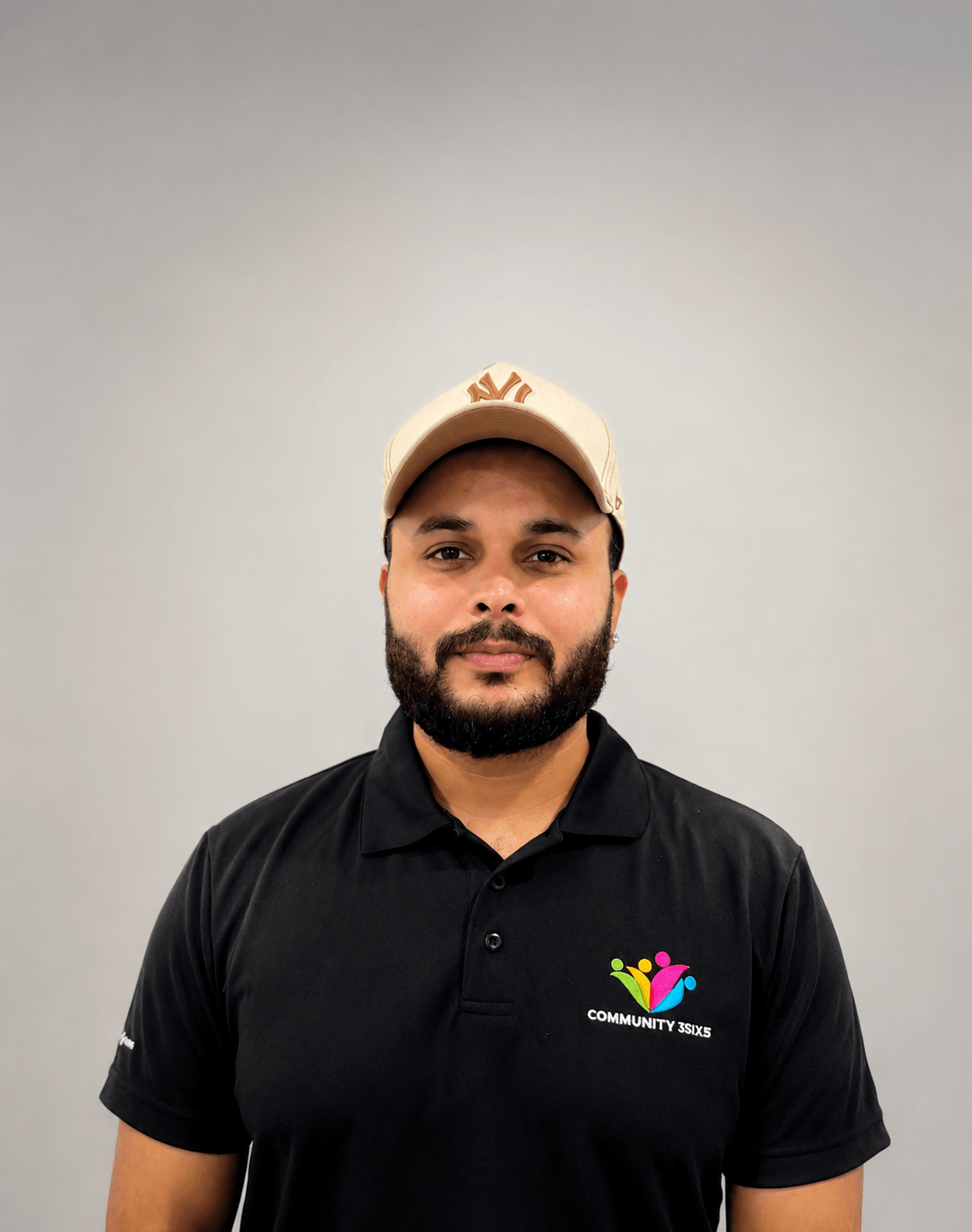 Navjot, staff member, wearing a black Community3six5 polo shirt and beige cap, smiling at the camera.