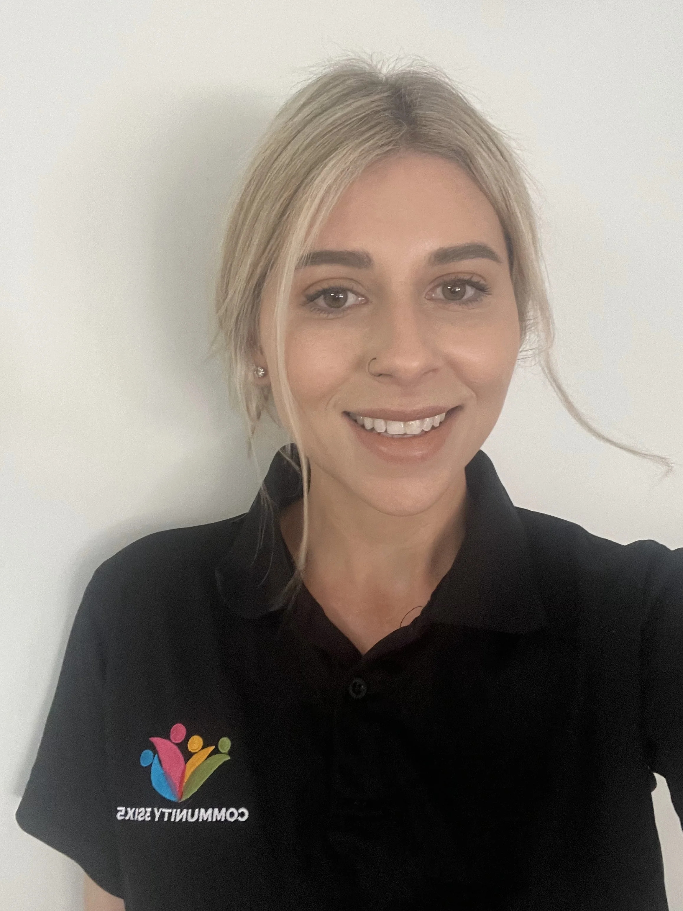 Female staff member Jill. She has long straight blonde hair in a pony tail. She is wearing a black uniform polo shirt and she is smiling.