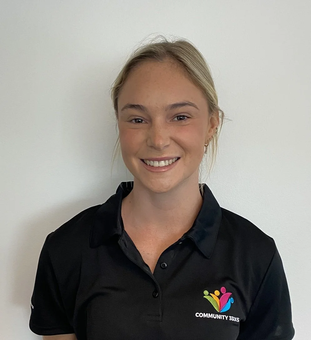 Female staff member Tayla. She has long blonde hair tied back in a pony tail, she is wearing a black uniform polo shirt.