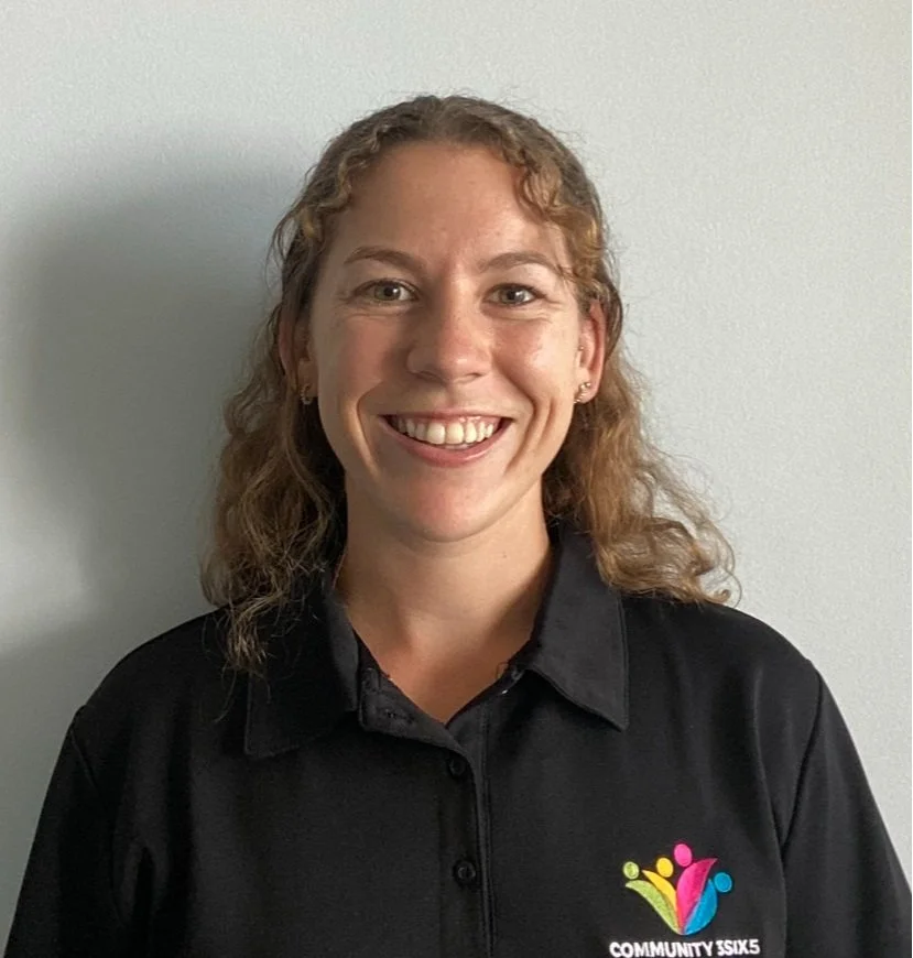 Female staff member Claire, she has curly shoulder length light brown hair. She is wearing a black uniform polo shirt and she is smiling.