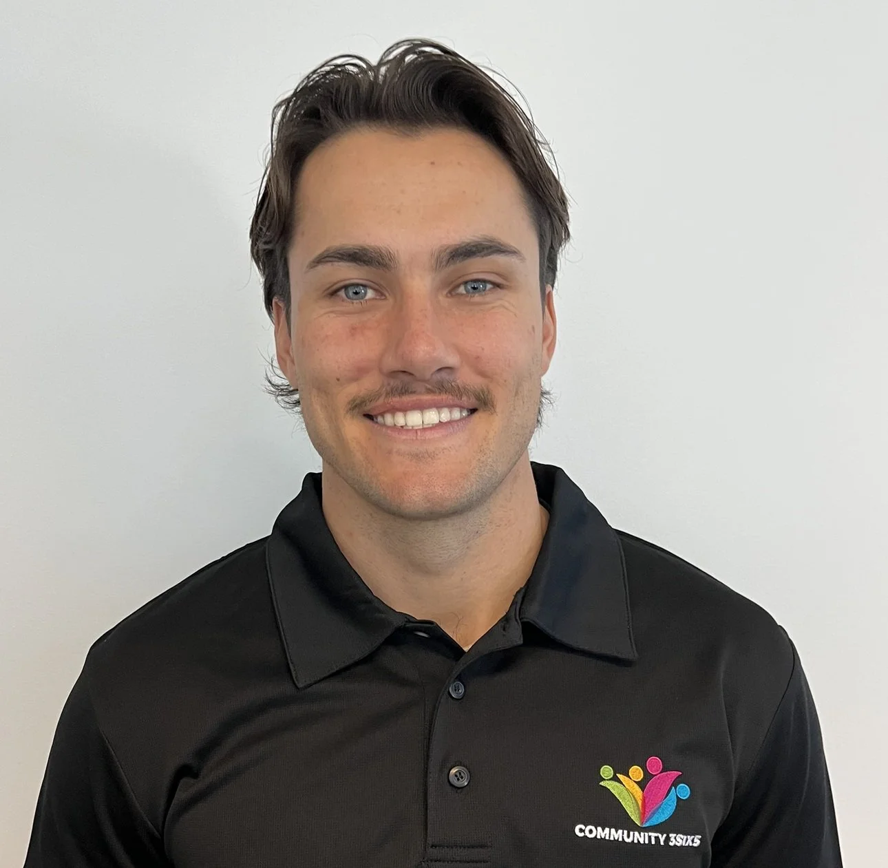 Male staff member Kristian, he has short brown hair and a short brown moustache. He is wearing a black uniform polo shirt and he is smiling.