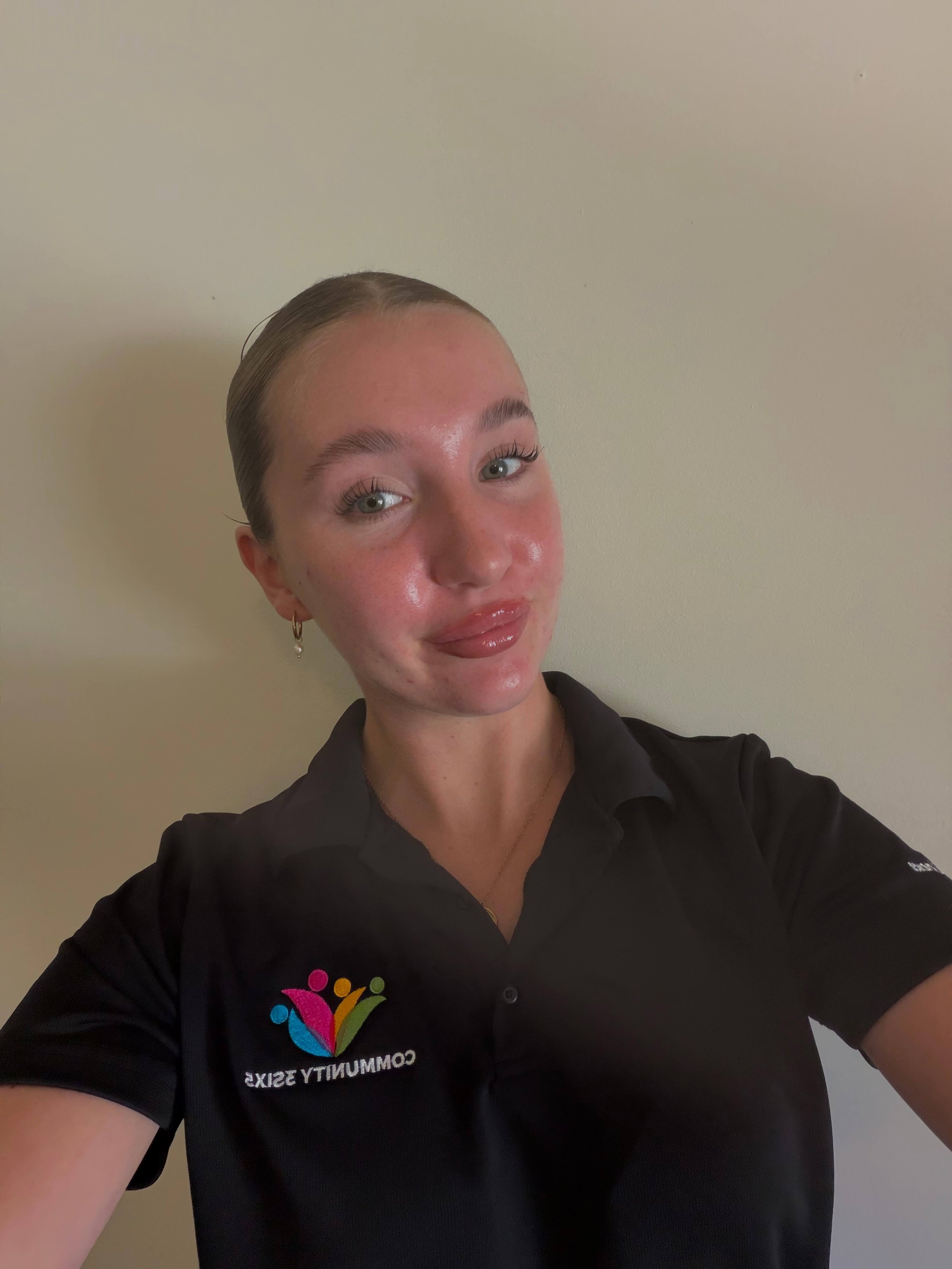 Charlotte smiling gently at the camera while wearing the black Community3six5 polo uniform, representing a professional and friendly NDIS support worker.