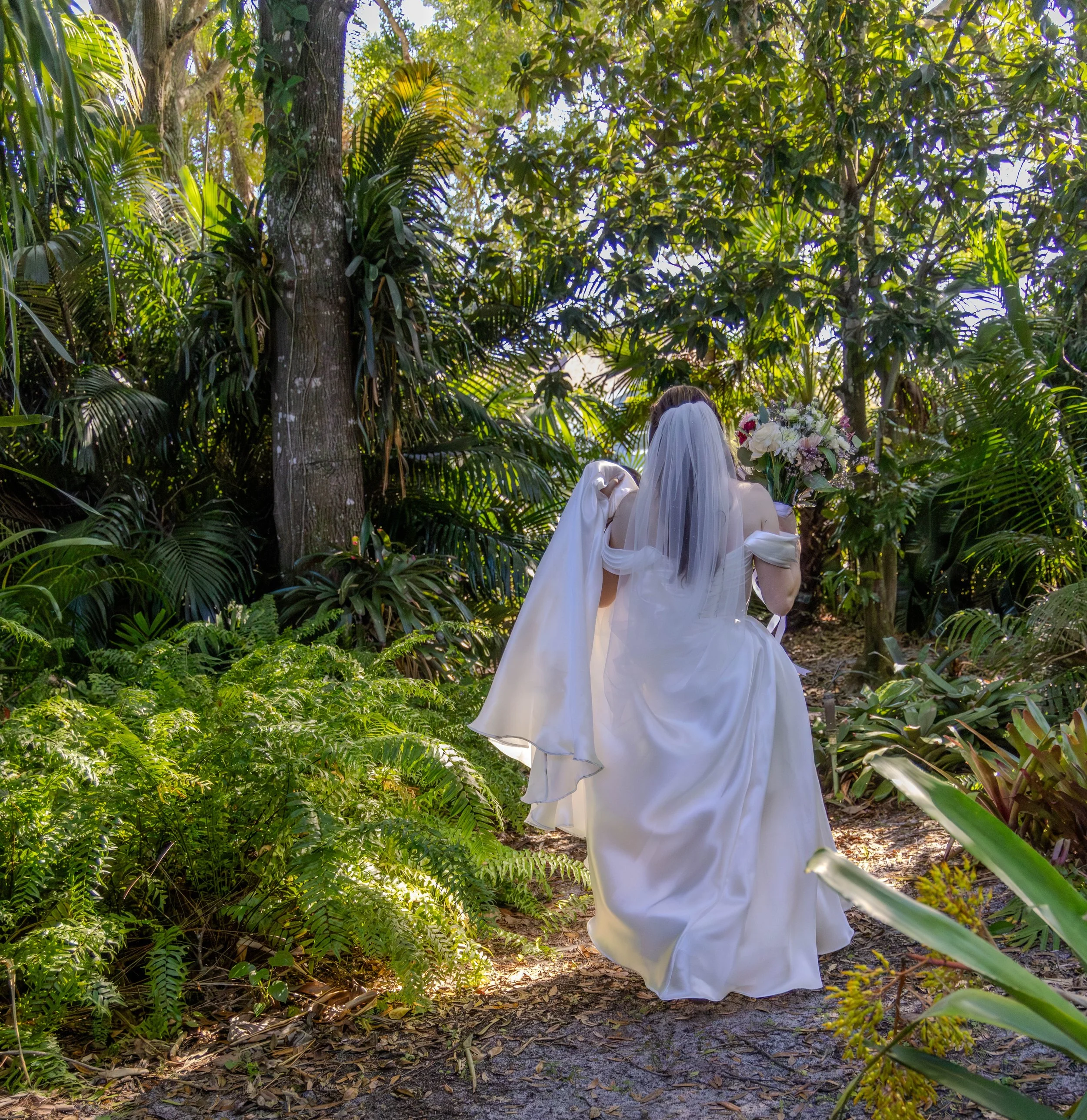 Couple walking through tropical greenery during their wedding portraits. 