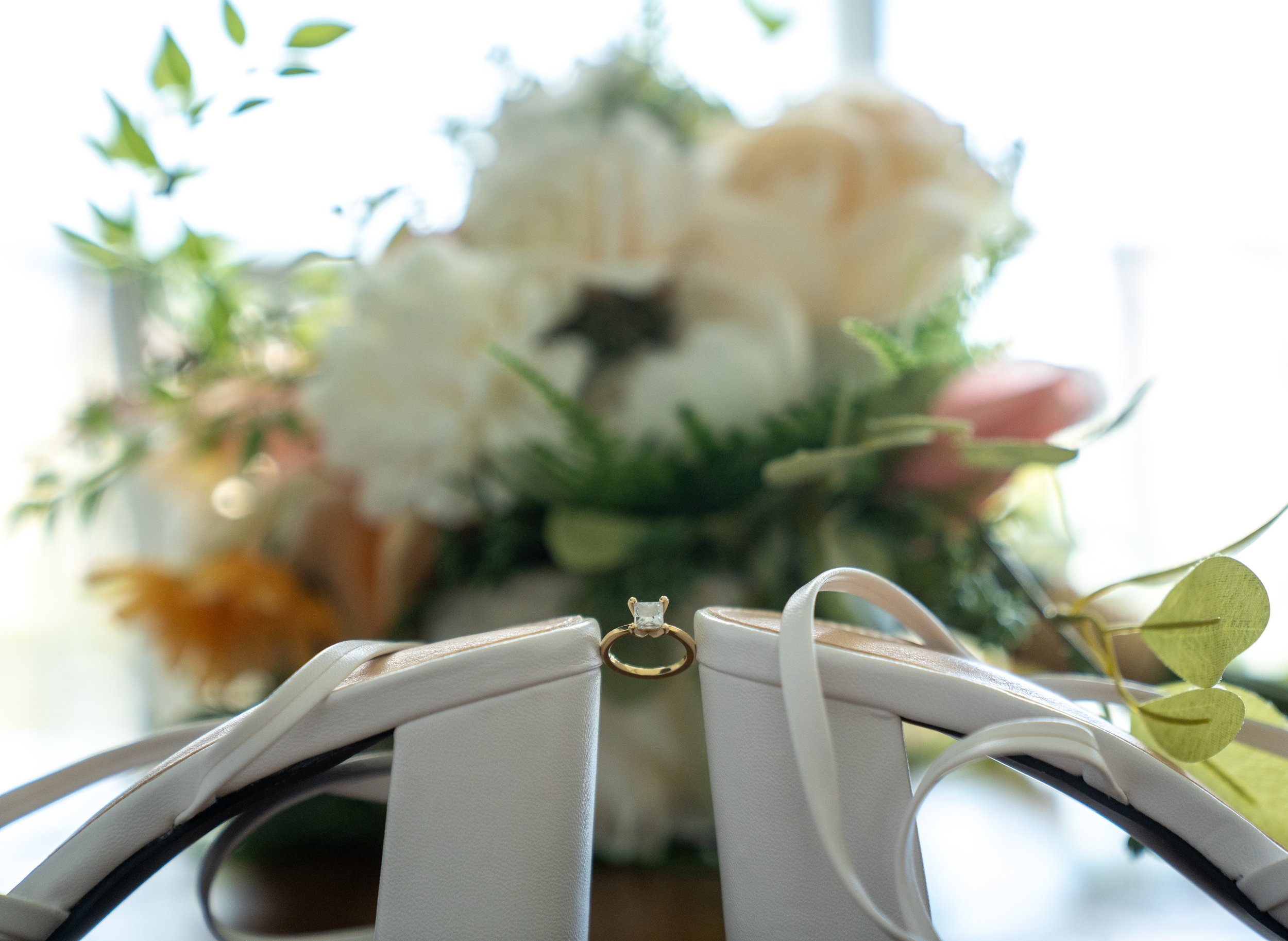 The bride’s wedding day details — her bouquet, the ring, and a pair of heels waiting by soft morning light
