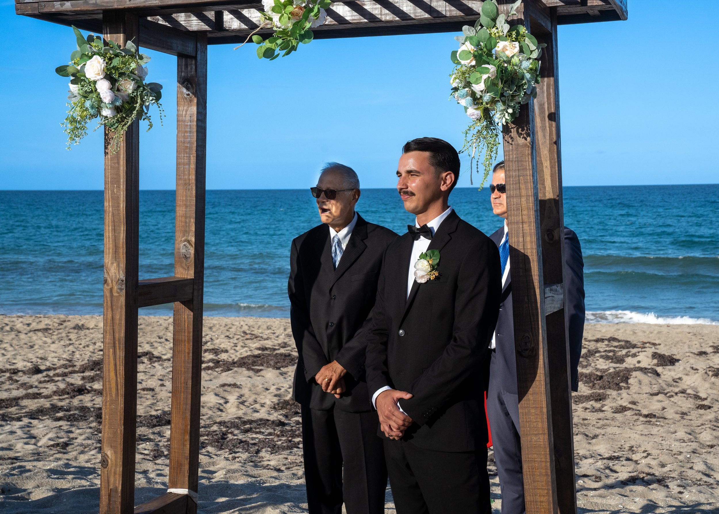 The groom and officiant await with the ocean as their backdrop