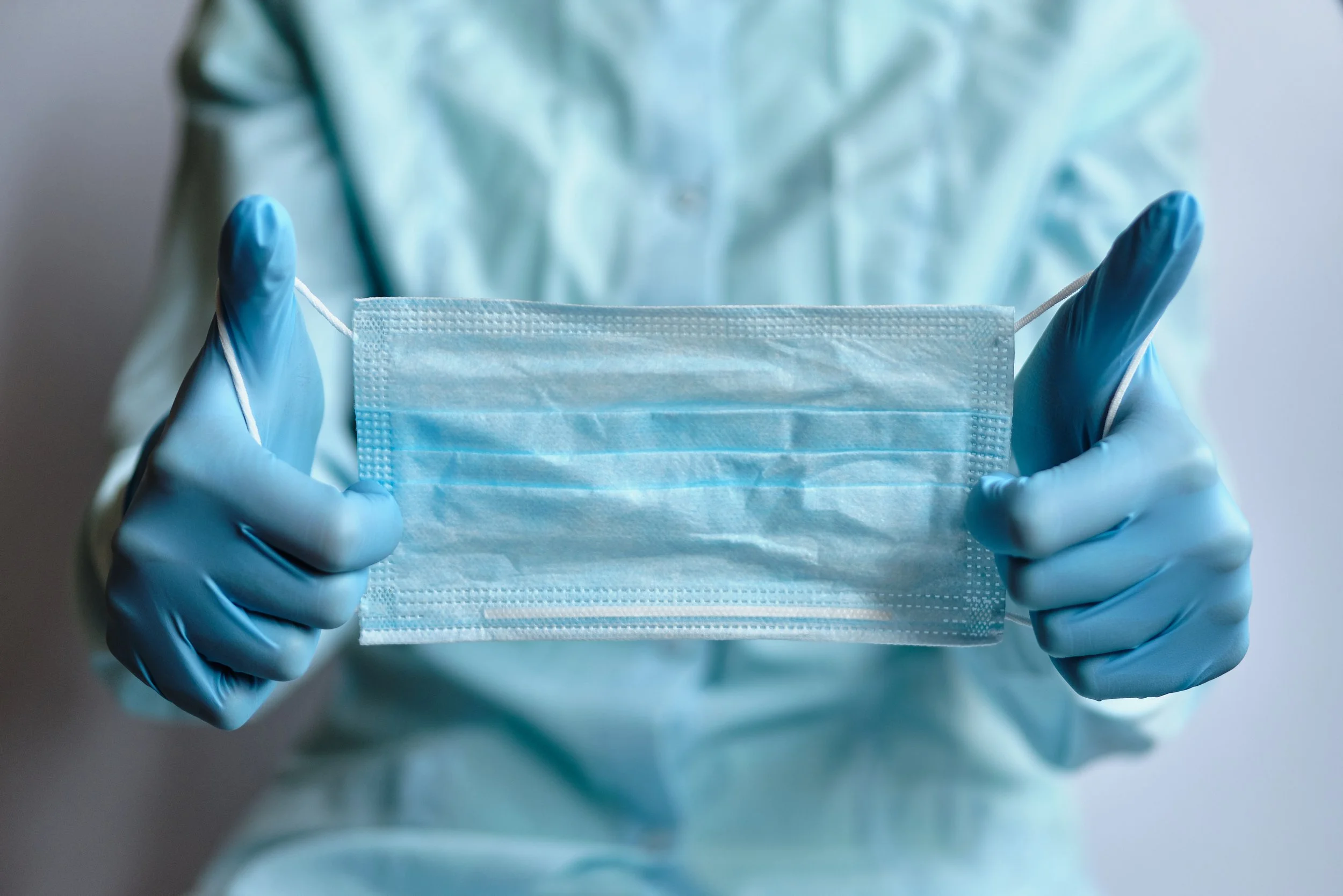 Person in protective gloves holding a blue disposable face mask.