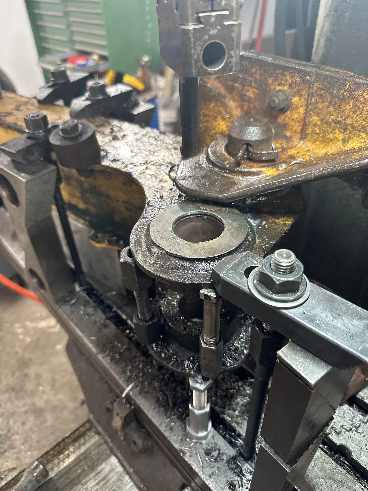 Close-up view of machine parts, including a bearing, bolts, and metal components, with some rust and oil residue, in a workshop setting.