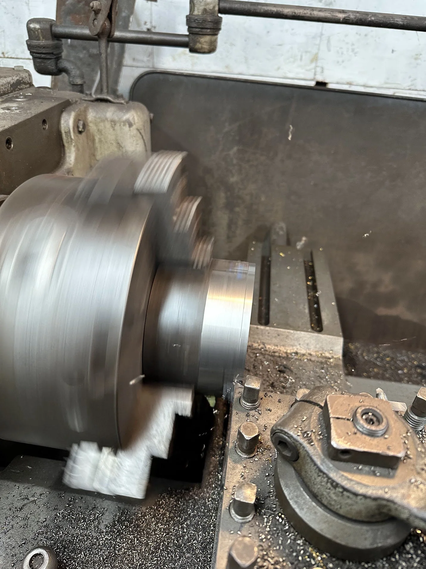 A metal lathe machine shaping a cylindrical metal piece, with metal shavings around the workspace.