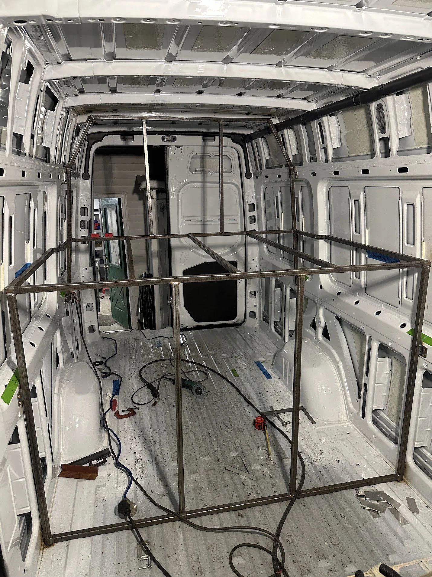 Interior of a van under construction with metal frames, tools, and wiring visible inside.
