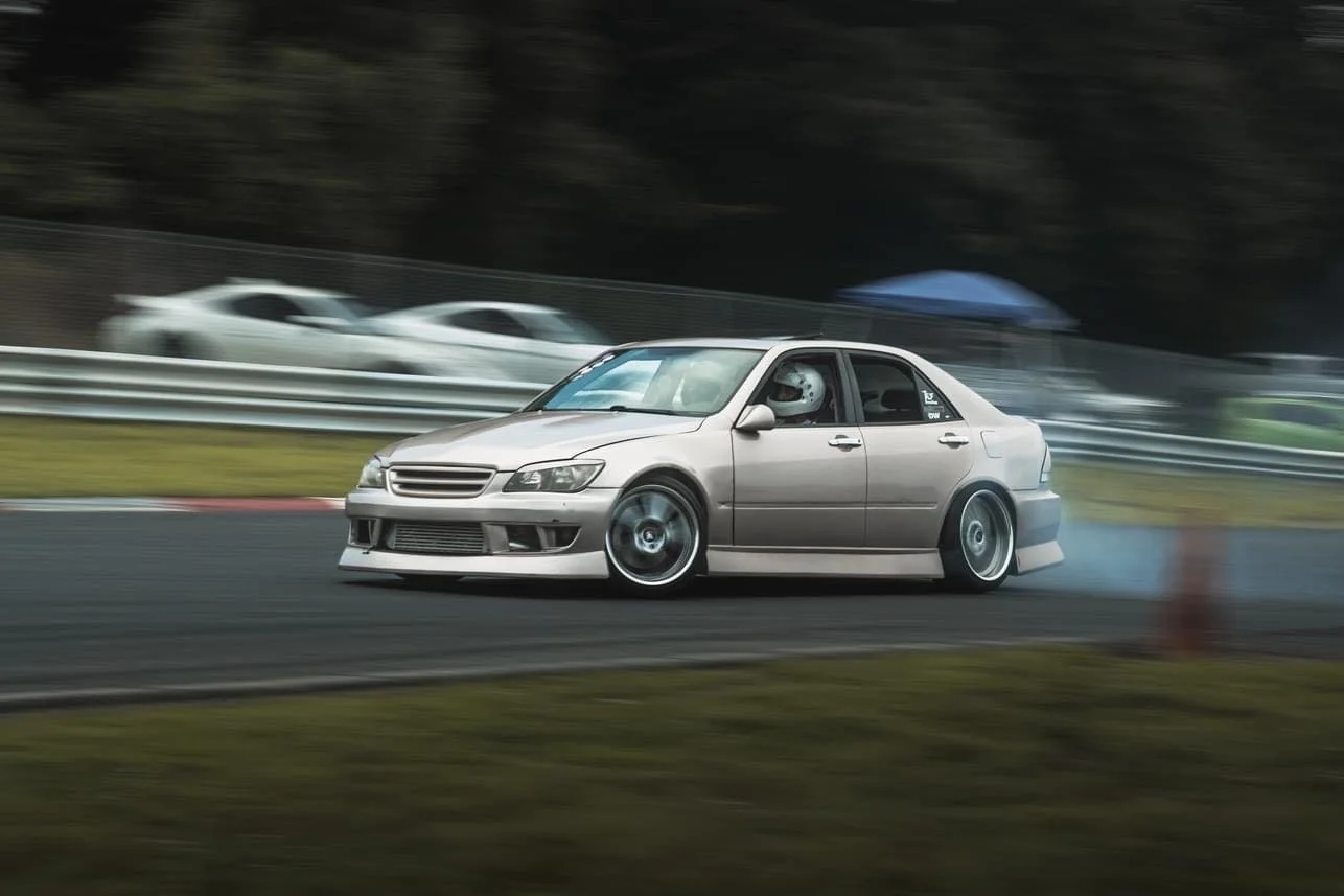 A silver race car drifting on a race track with blurred background and tire smoke.