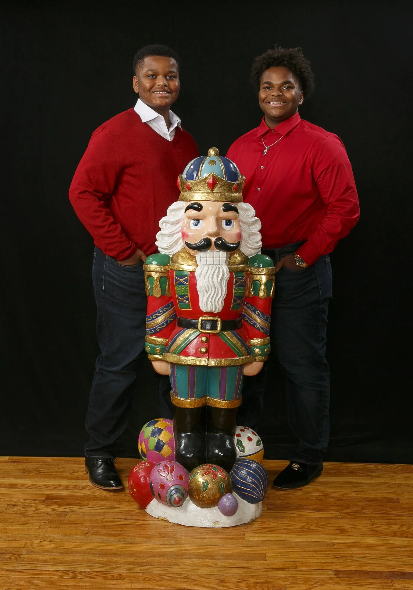Father and son  in red sweaters posing with a whimsical stacked Christopher Radko nutcracker sculpture in front of a black background during a Hayes & Fisk holiday studio session.
