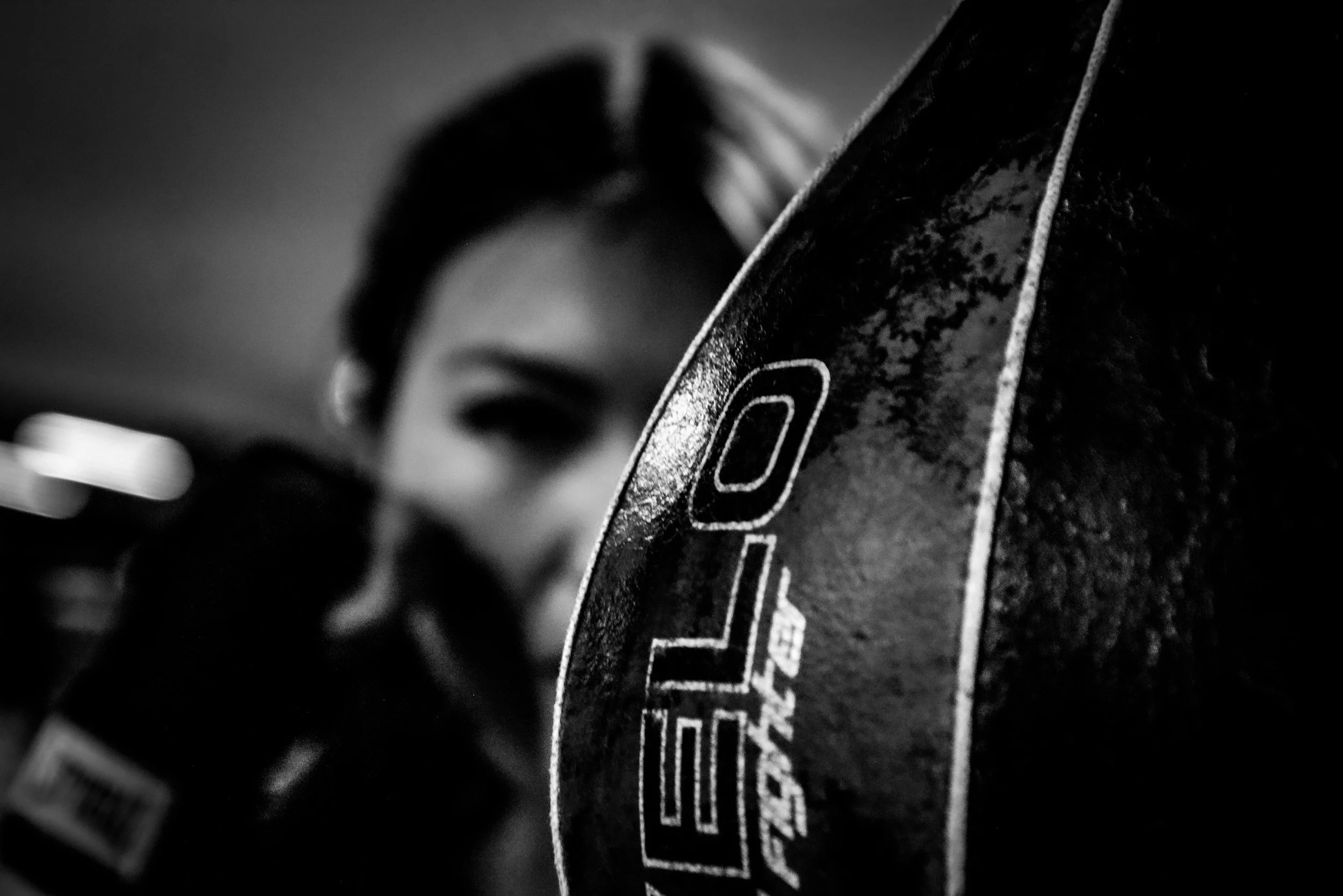 Close-up of a black and white photograph showing a section of a bicycle tire with textured sidewall and tread pattern, and part of a person's face with hair blurred and out of focus in the background.