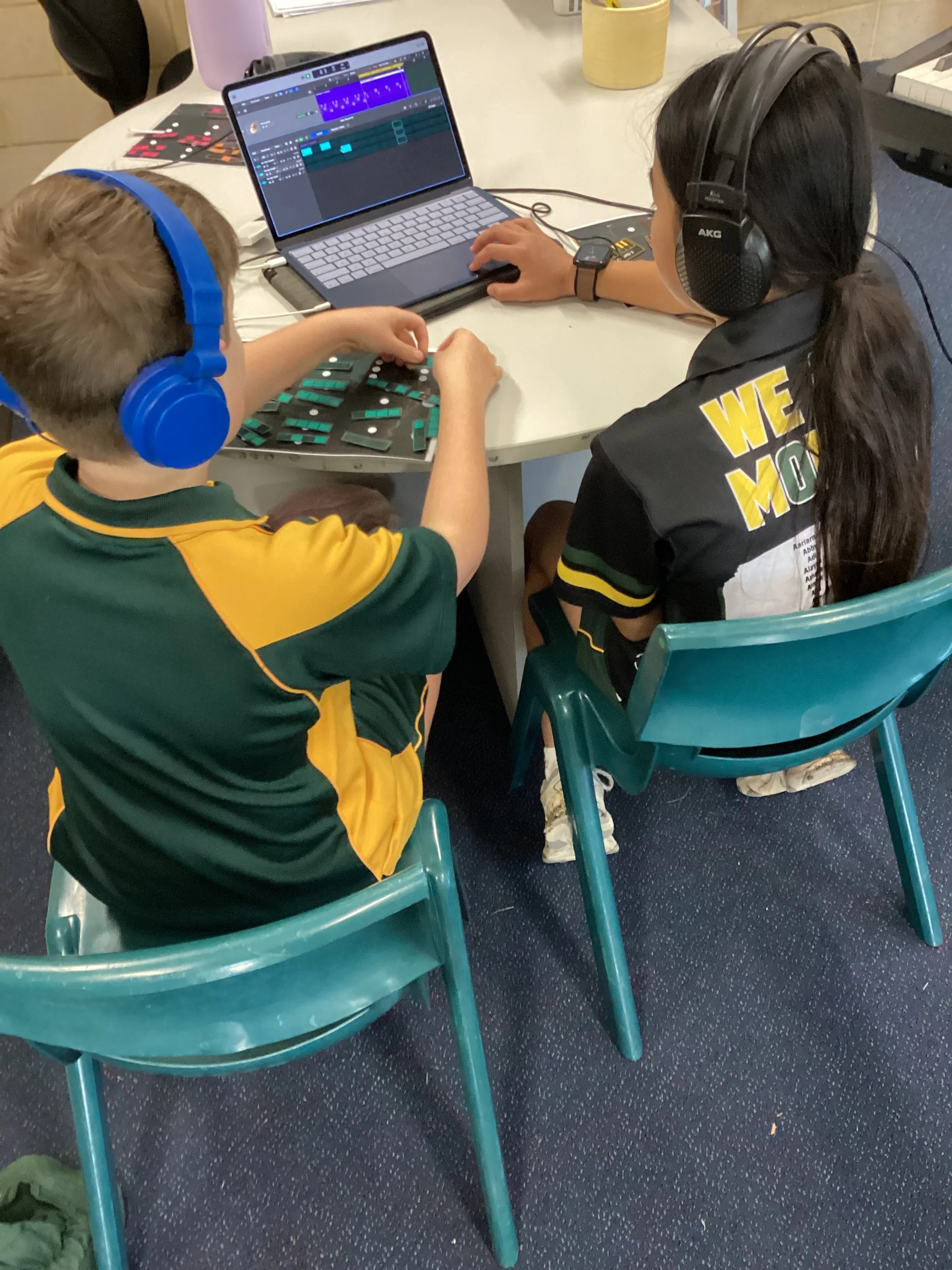 Person wearing headphones playing keyboard connected to a computer with music software display.