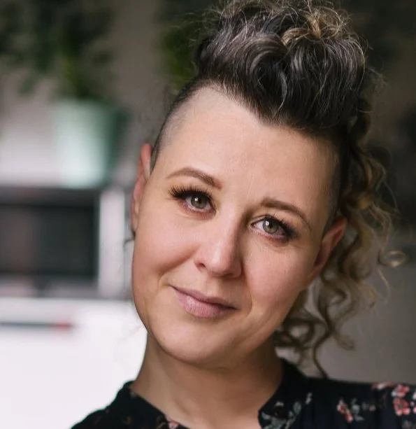 Scenic landscape with a calm lake in the foreground, surrounded by green hills and rugged mountains under a cloudy sky.