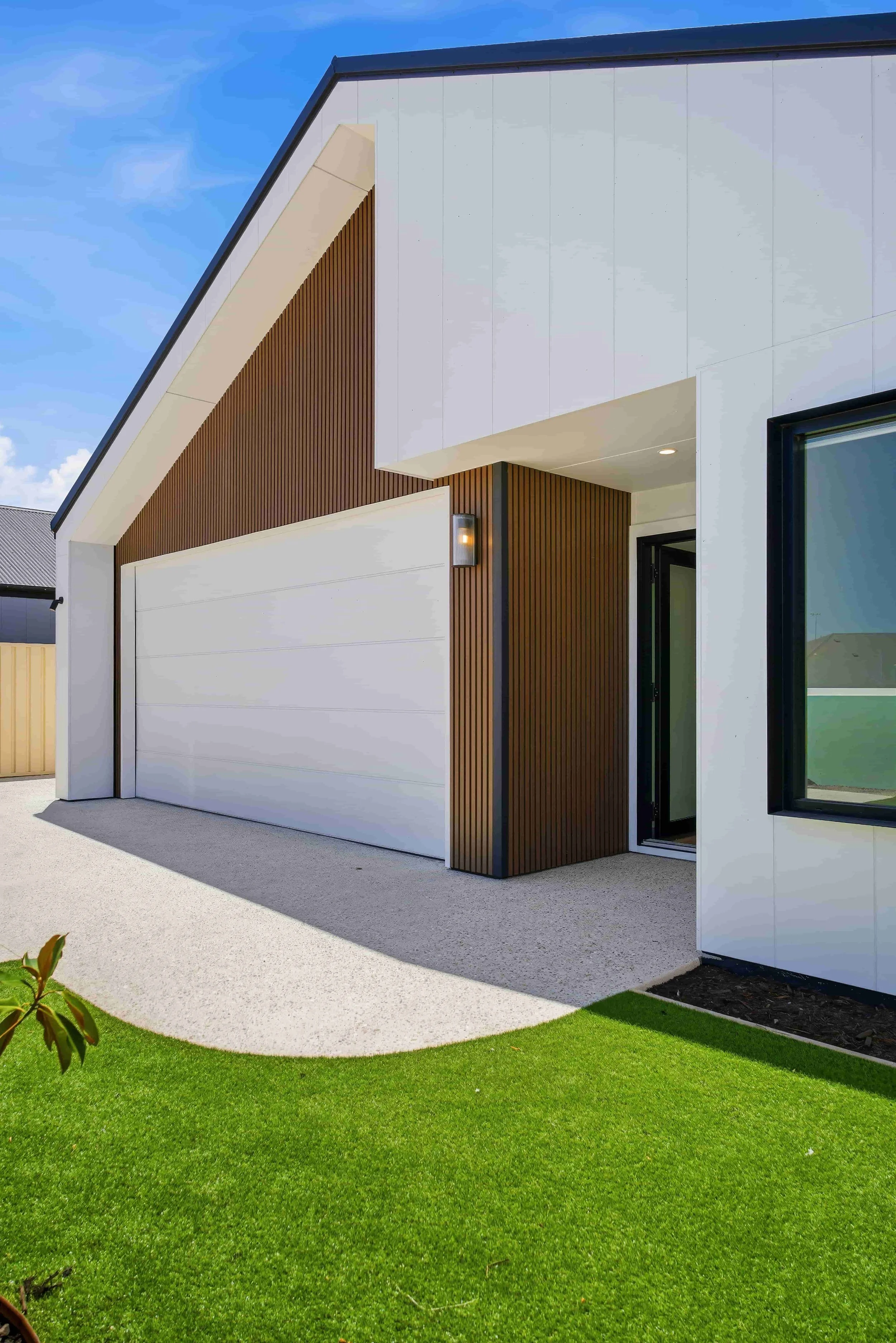 Modern house exterior with white and wood siding, large garage door, black window frame, and green lawn.