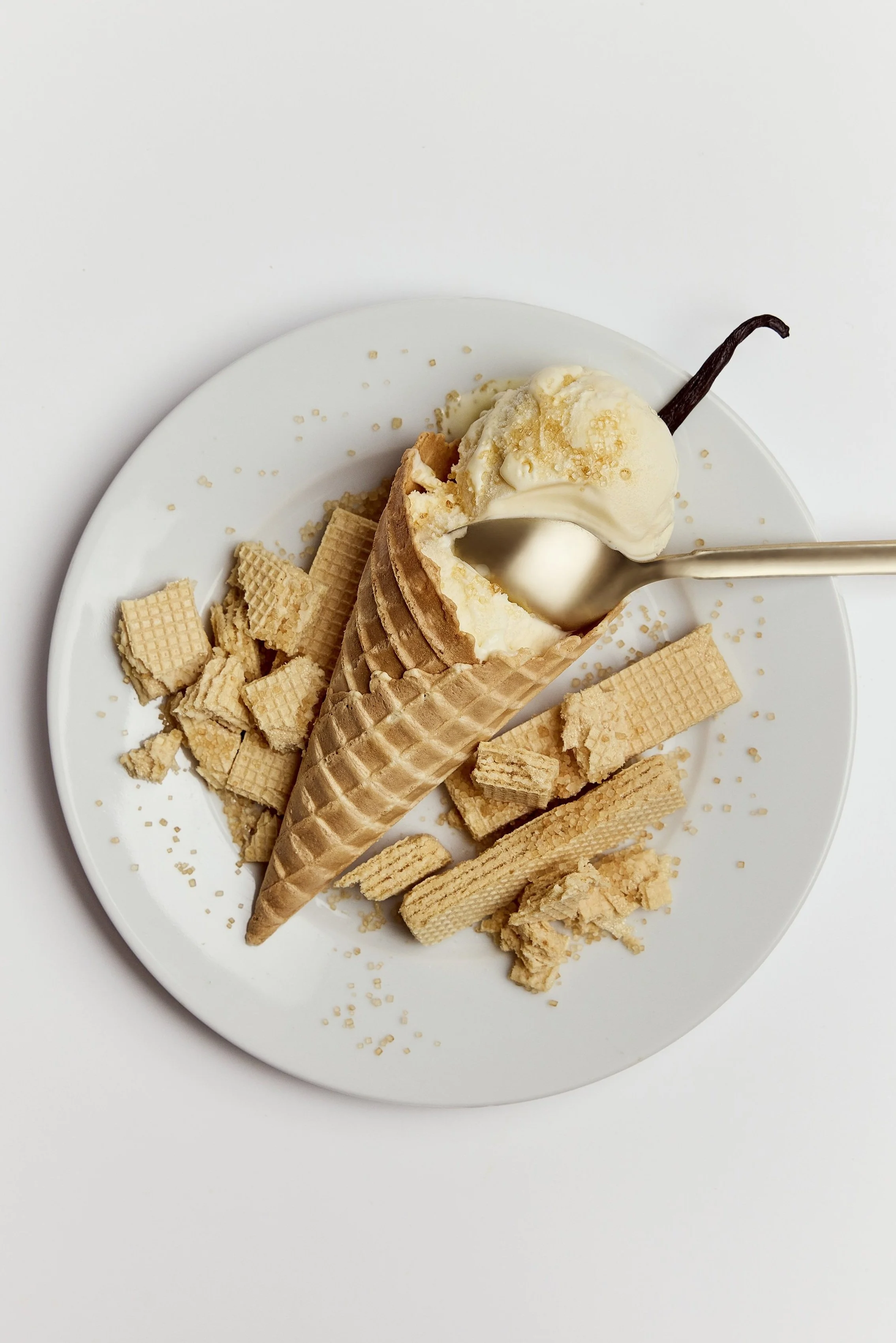 Vanilla ice cream in a waffle cone with crushed biscuits on a white plate.