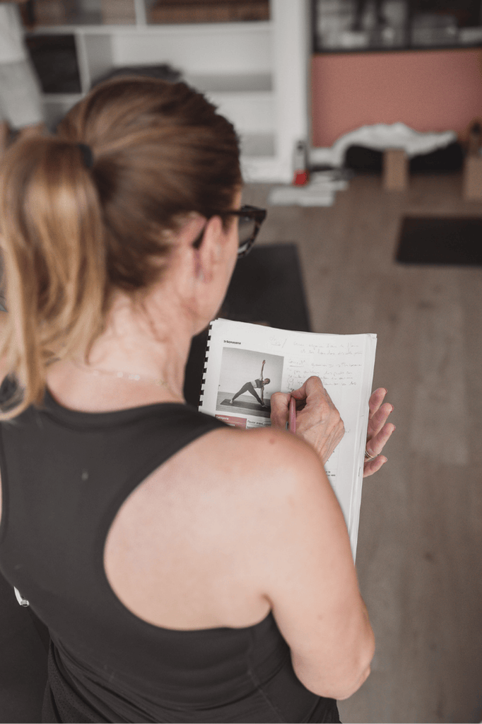 femme en train de prendre des notes sur son manuel de formation de yoga