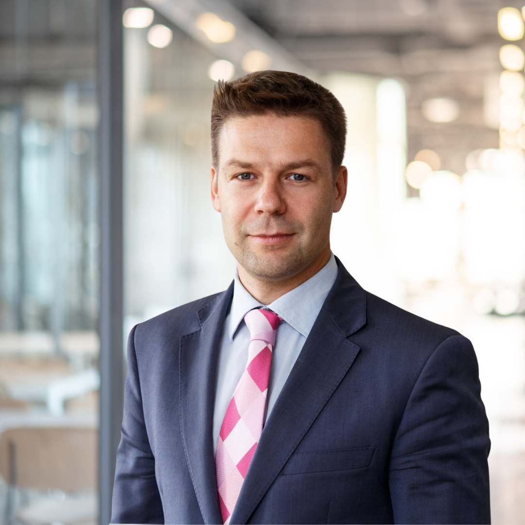 Mand i forretningspåklædning med blå blazer og pink ternet slips står i et kontormiljø