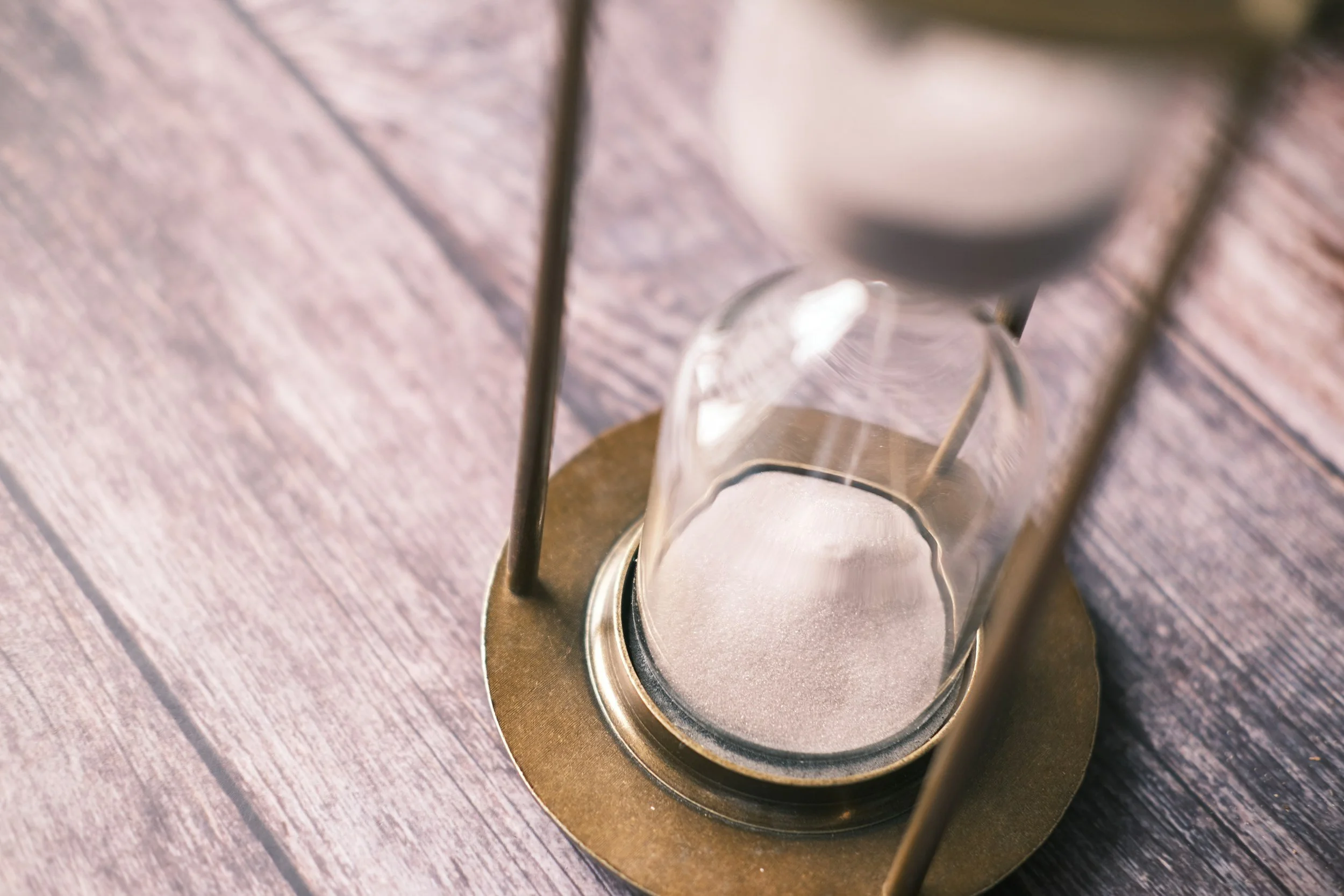 Close-up of a sand timer with white sand inside, placed on a wooden surface.