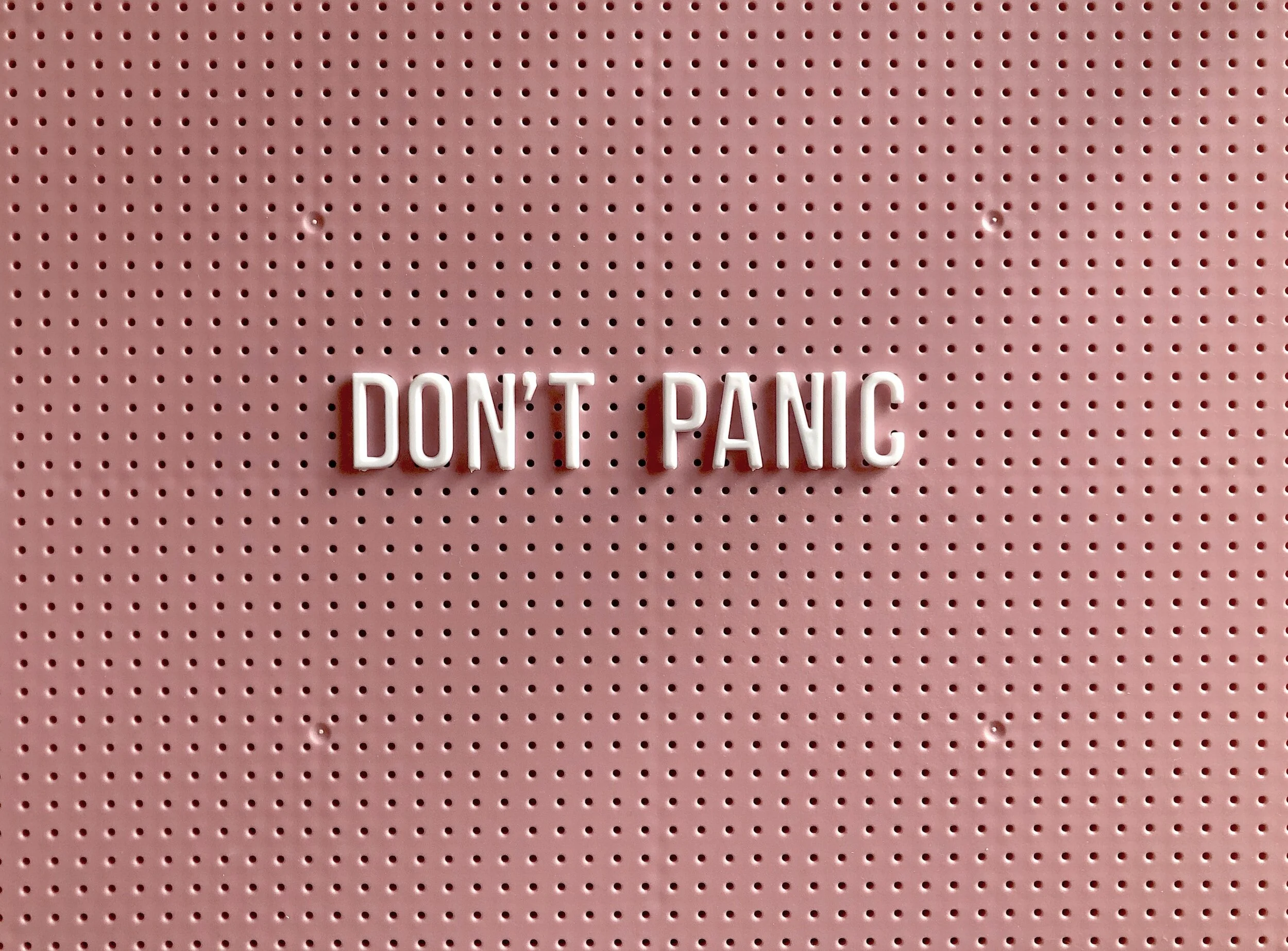 Pink pegboard with white letters spelling 'DON'T PANIC' in the center.