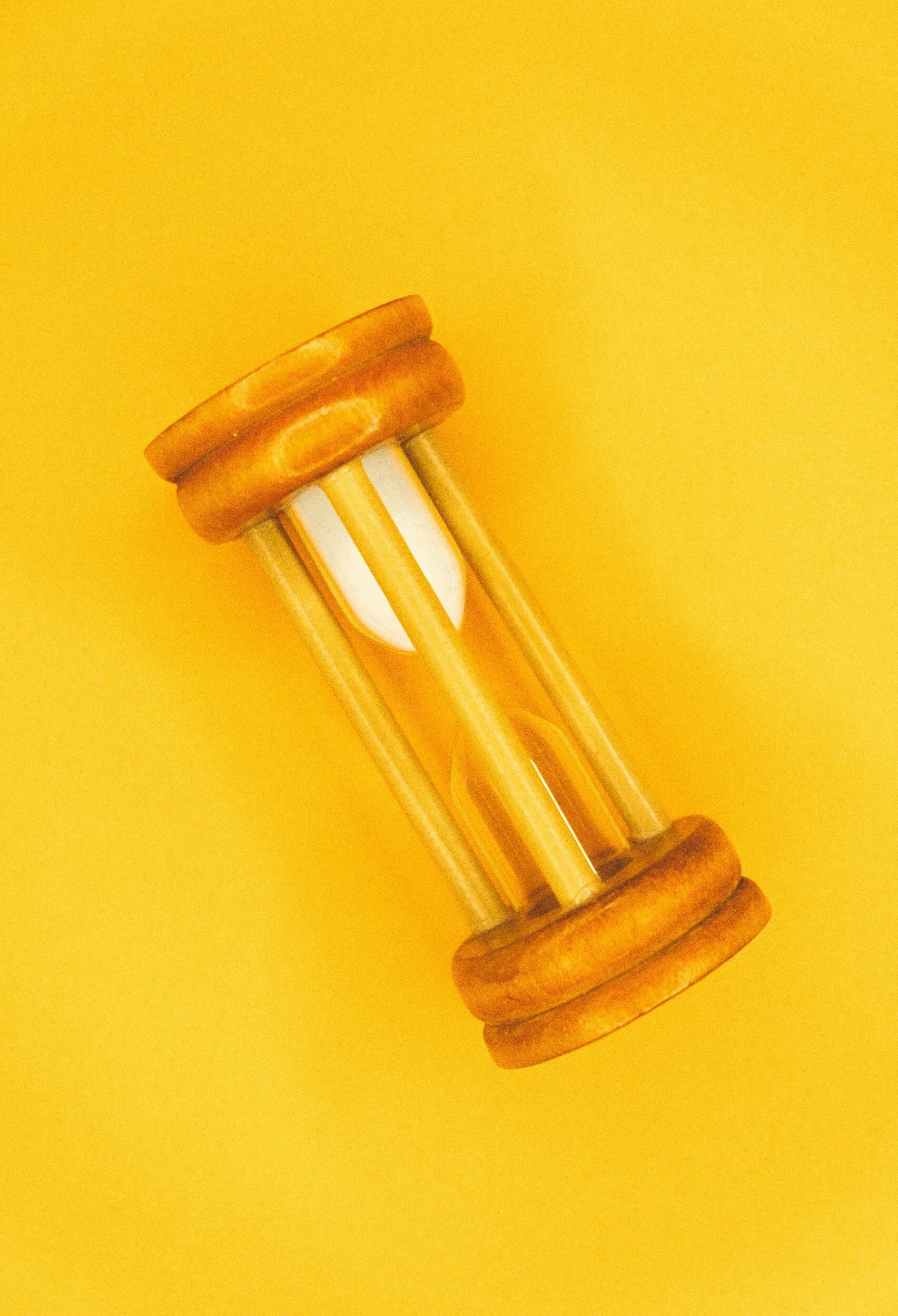Yellow background with a small wooden hourglass with glass center and sand inside.