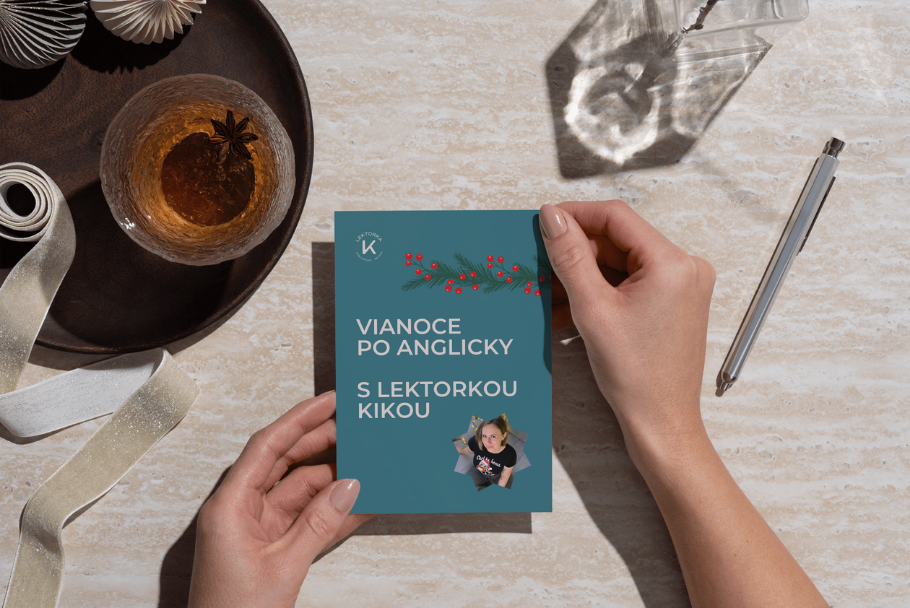 A person's hands holding a Christmas card on a marble table. The card features holiday decorations, a photo of a woman, and Czech text. Nearby are a glass of drink with a star anise garnish, a pen, and a decorative ribbon.