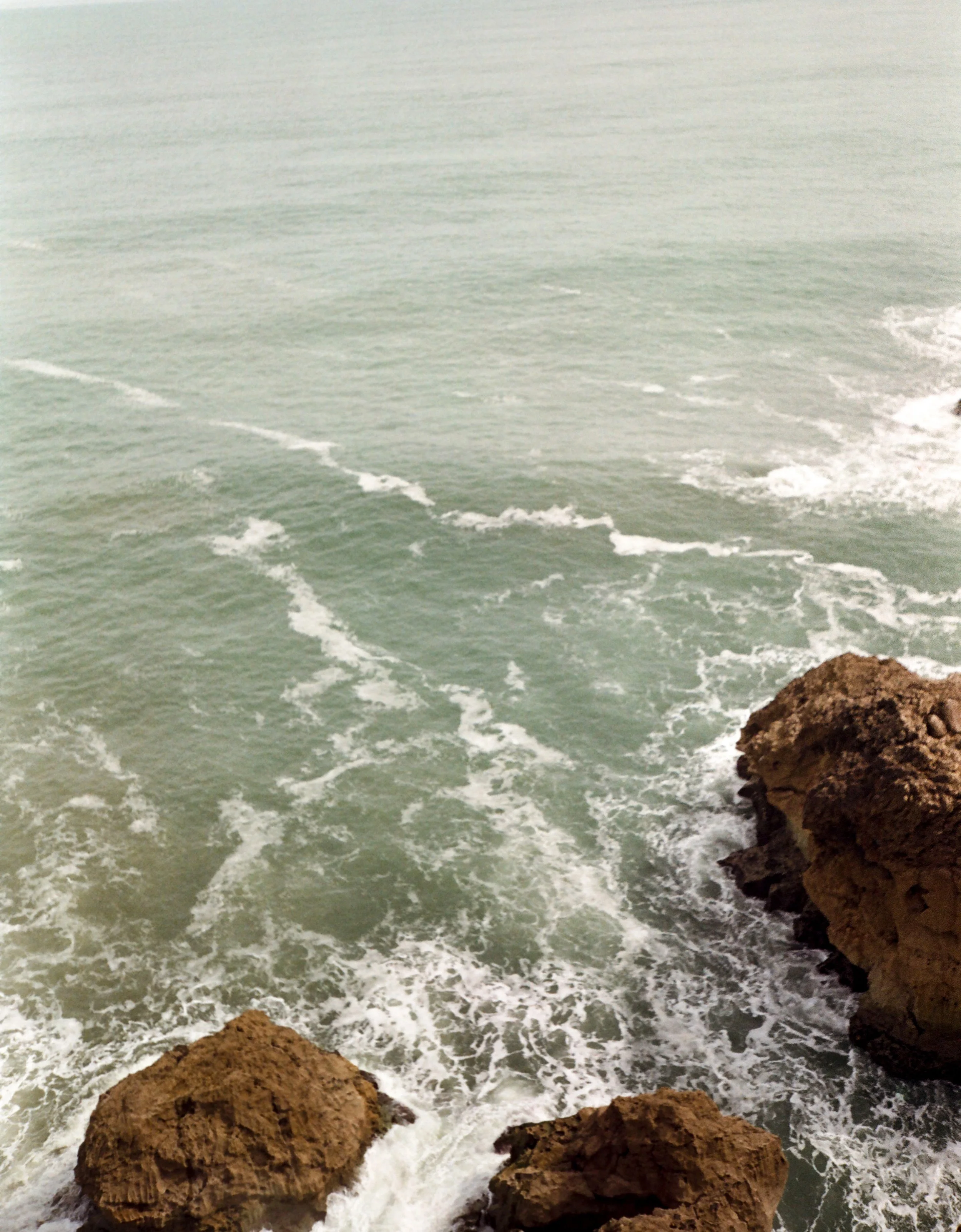 Ocean waves crashing against rocks on a cloudy day.
