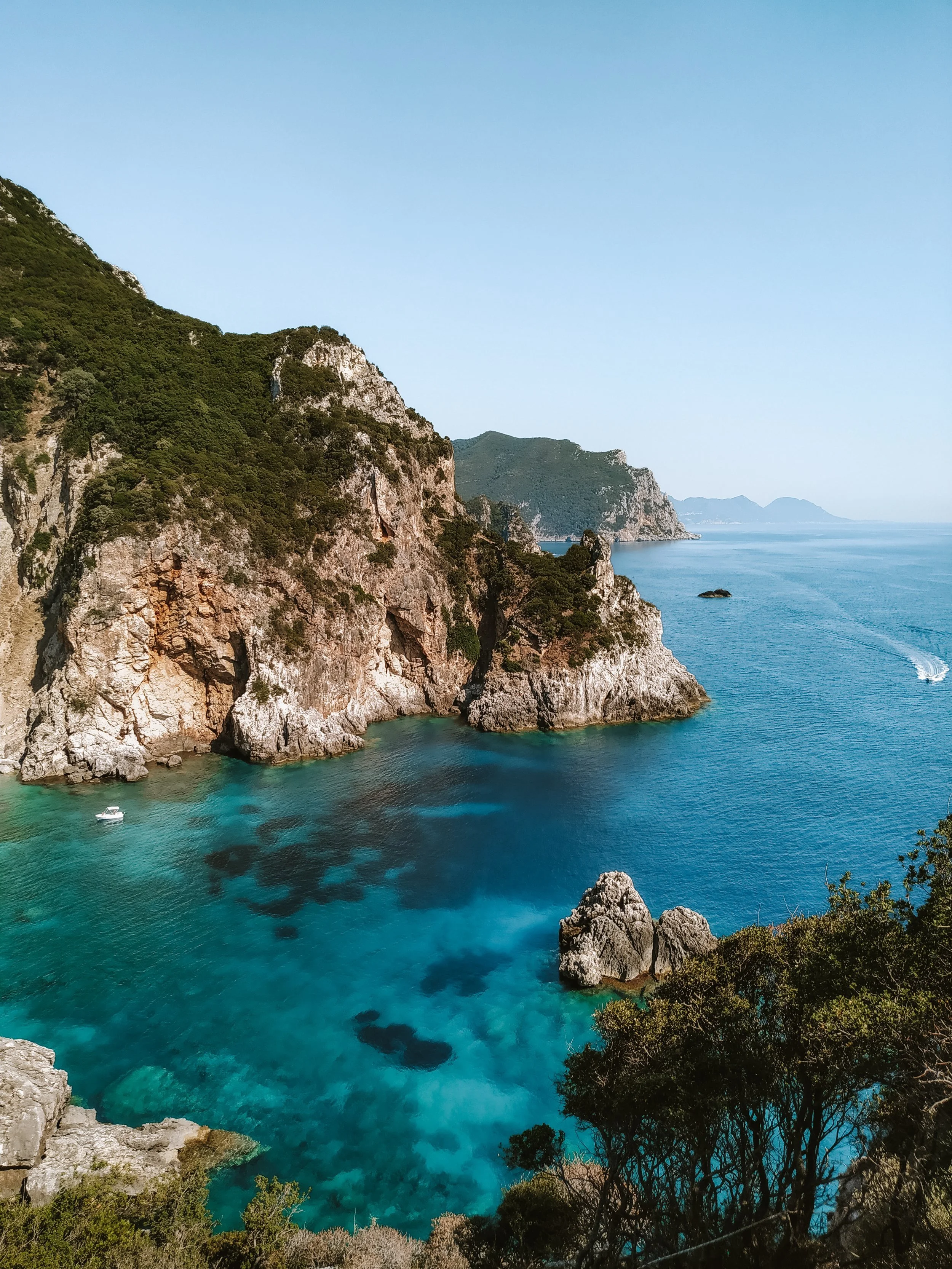 Coastal cliffs and turquoise waters, with boats and lush greenery.