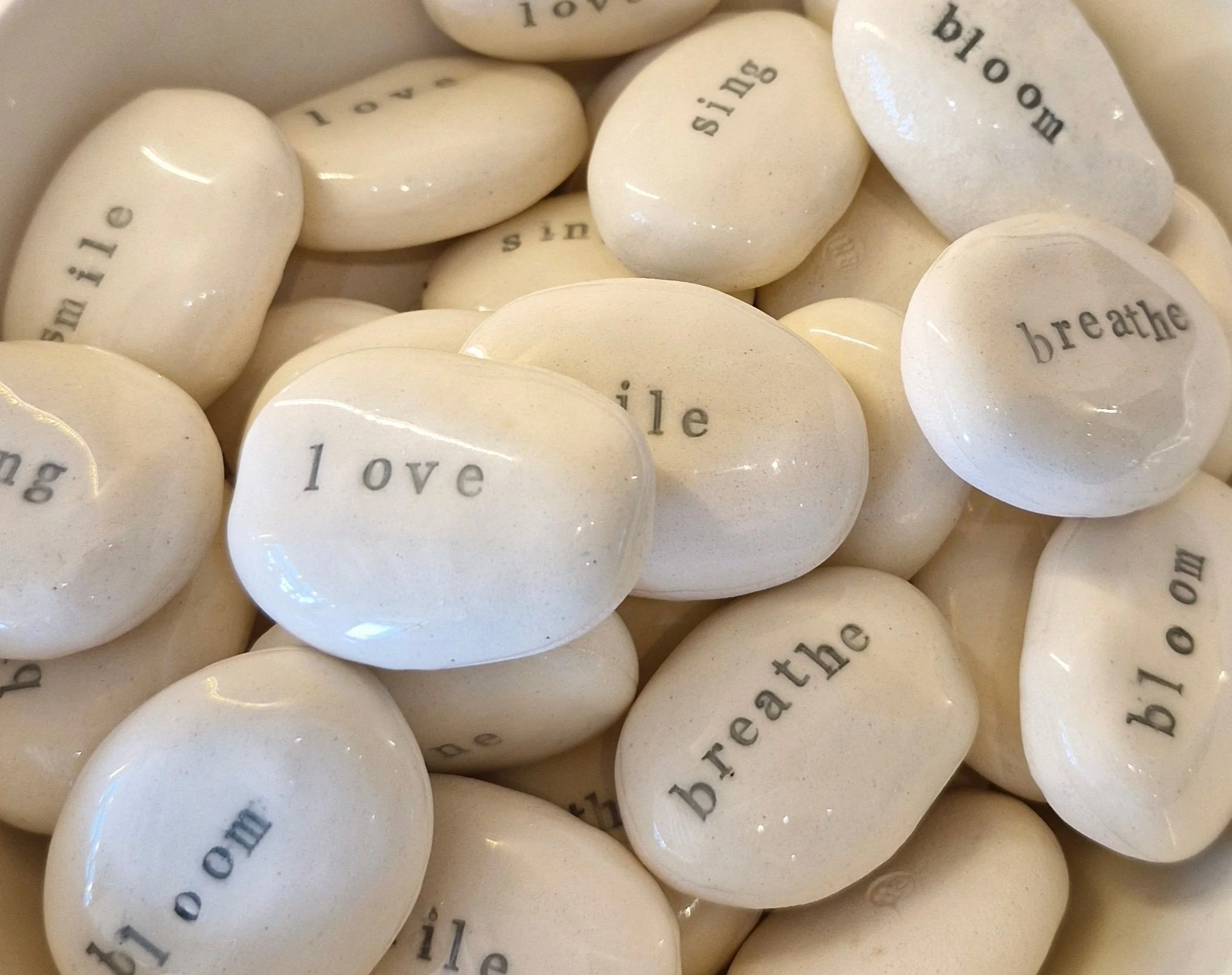Close-up of white oval stones with printed words like 'love', 'breathe', and 'smile' in black font.