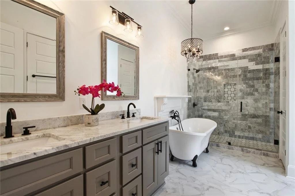 Step into our Valence St project's master bathroom! We&rsquo;ve kept the original mantle to preserve that classic New Orleans touch, and the charming bathtub is perfect for unwinding. The gray tile work and vanity create a seamless look. And who does