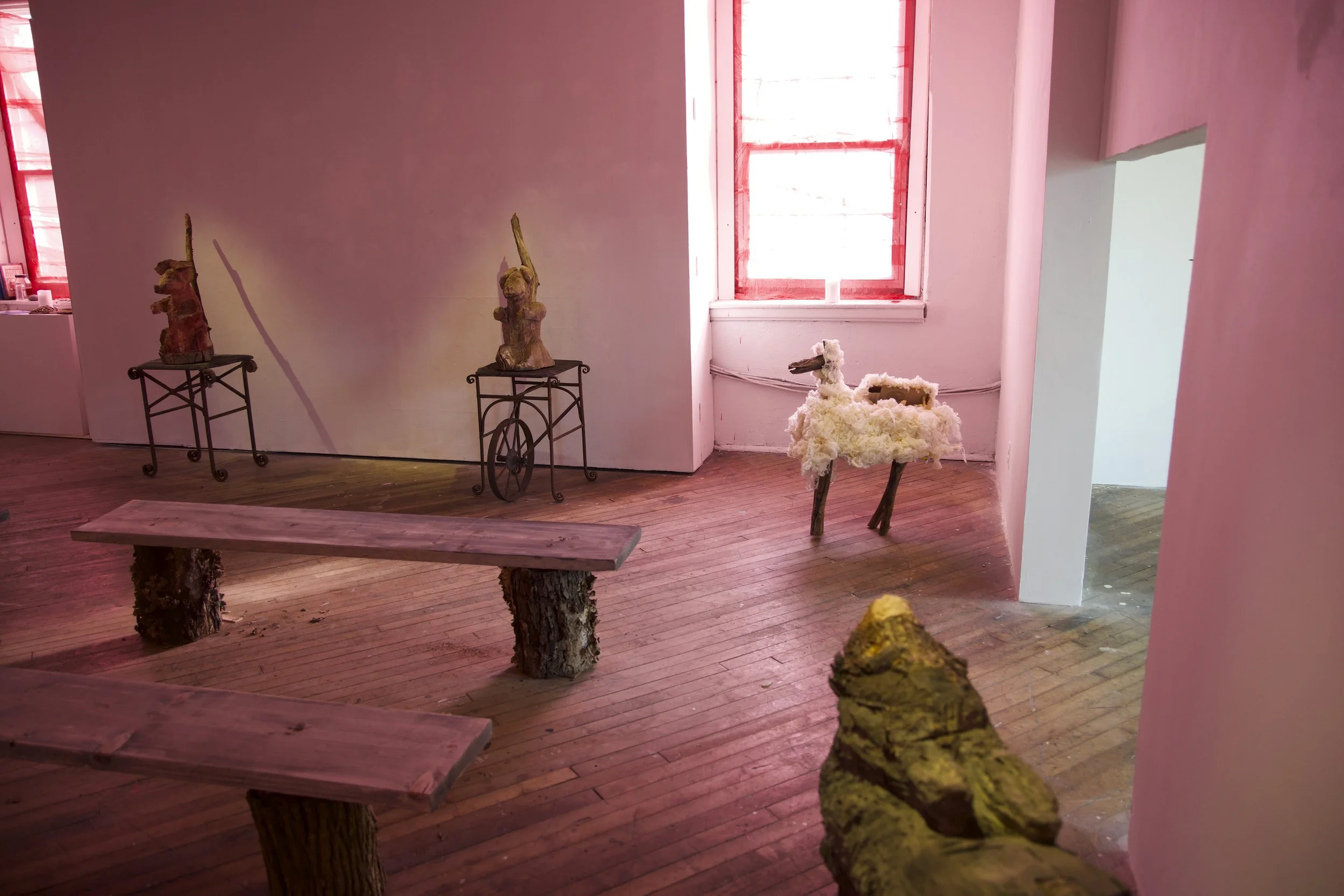 Installation View: Jim Strong’s reproduction of chapel pew’s adorned with animalistic sculptures and illuminated with pink light