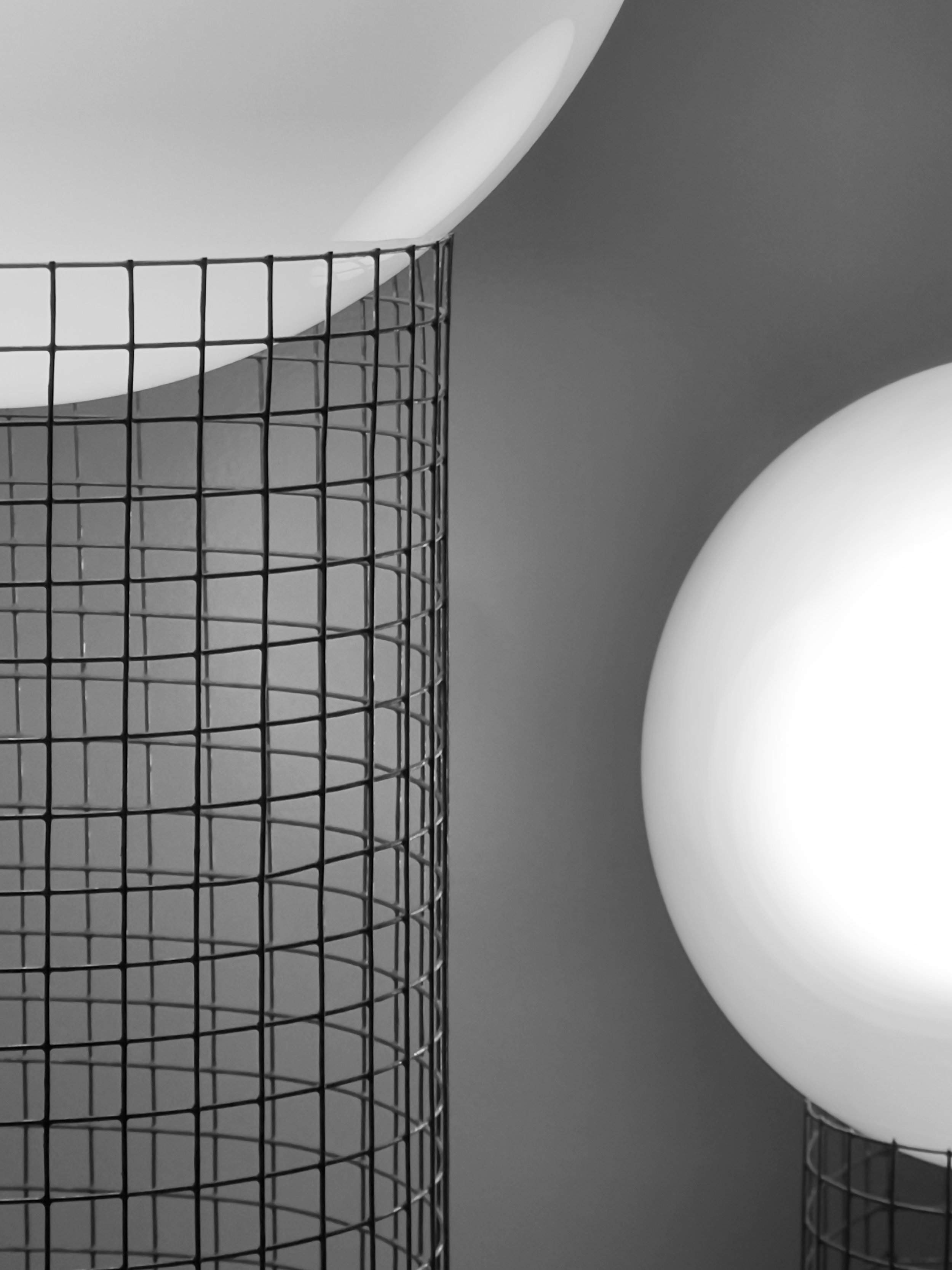 Black wire grid candle holder with a white candle inside, large white decorative sphere, and smaller wire sphere on a gray background.
Architecture and Design by Auliseo (Aurèle Eliseo Stauffer).