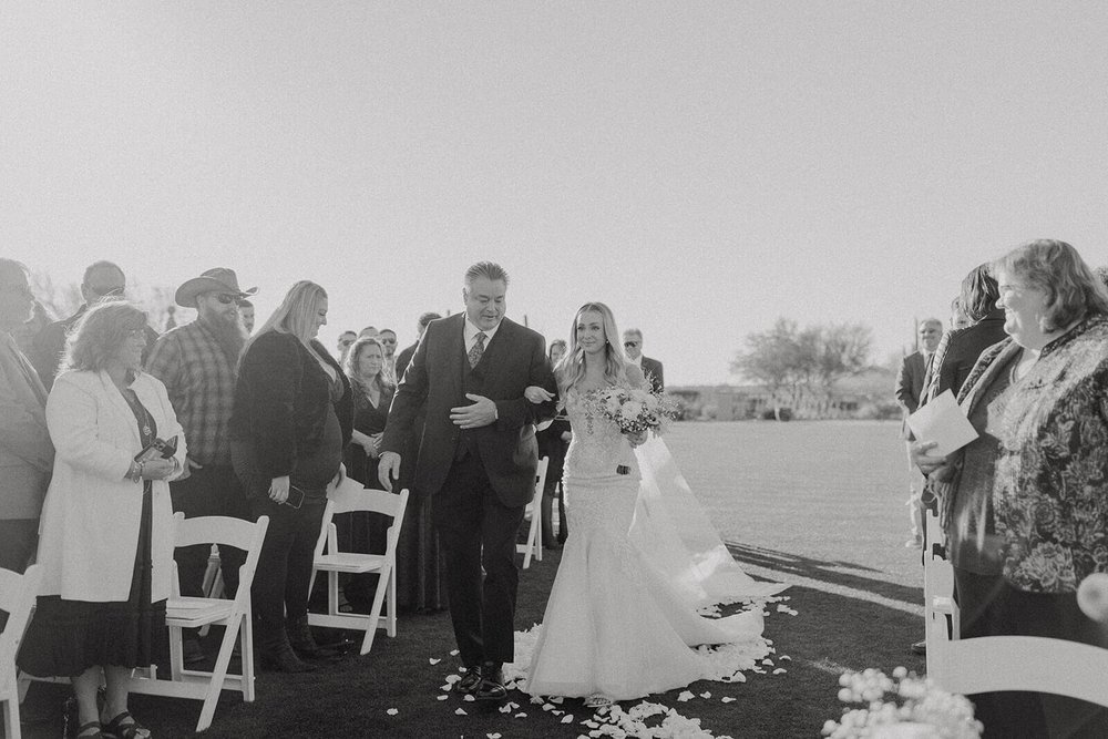 Black and white photo of bride walking down the aisle at an outdoor ceremony in Arizona