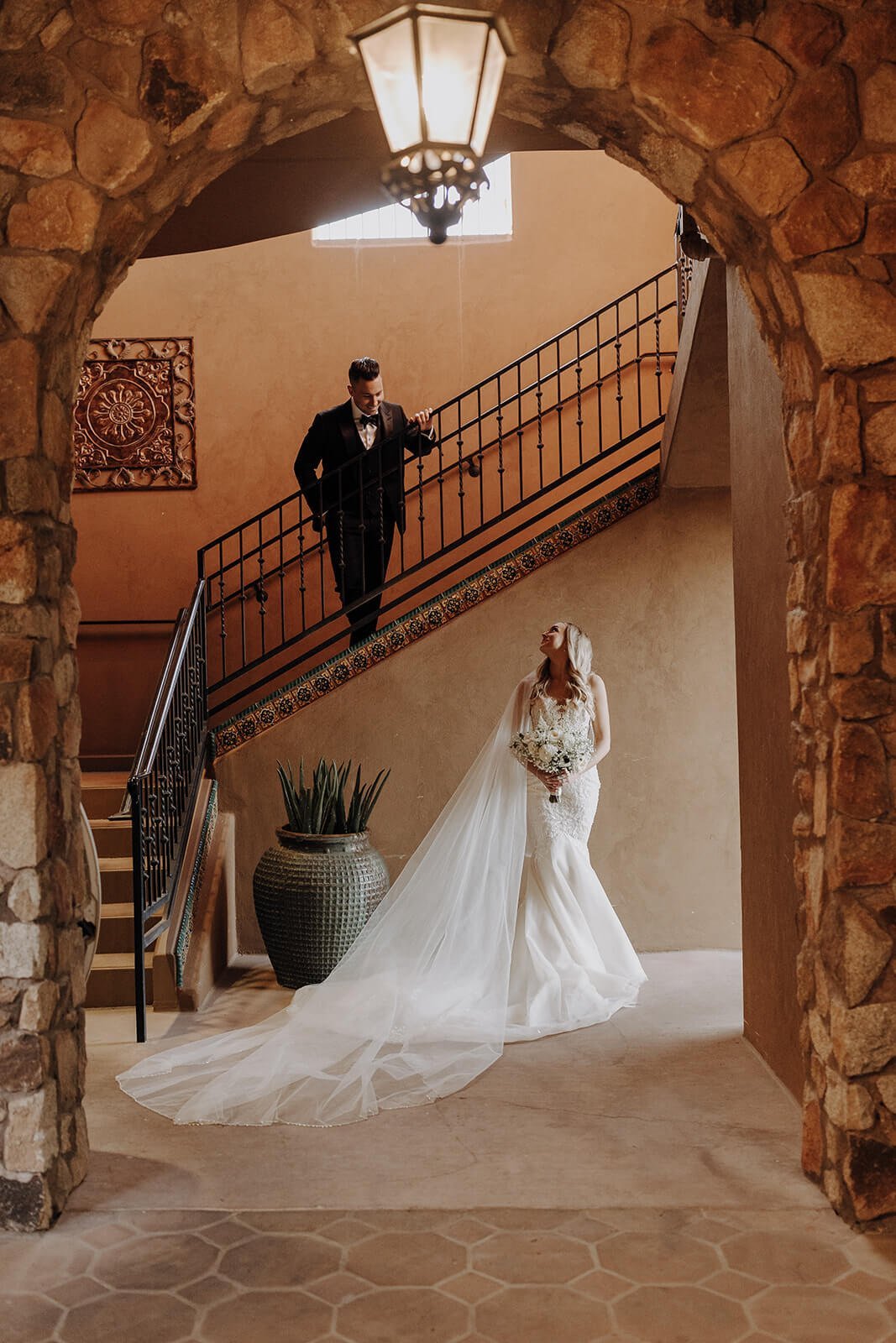 Groom standing on staircase, bride standing below in beautiful stone entryway at Blackstone Country Club in Arizona.