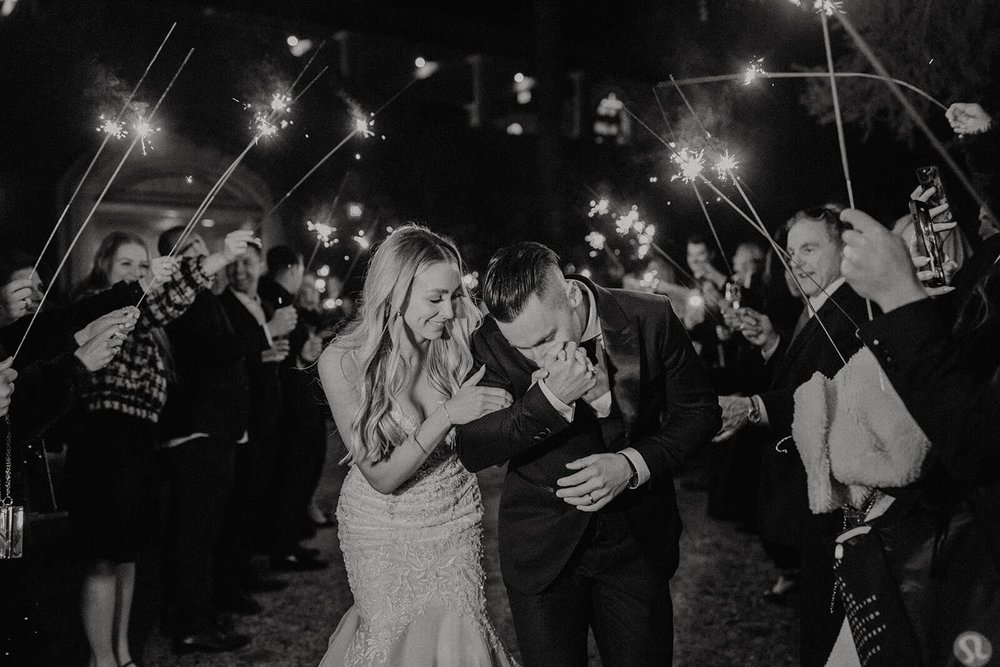 Groom kissing bride's hand at end of sparkler sendoff at classy black and white Arizona wedding